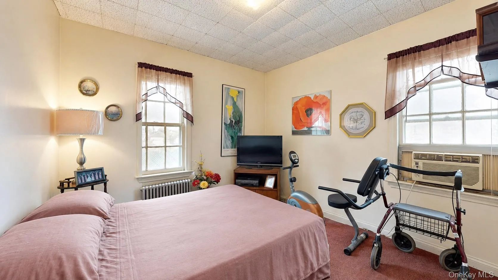 Interior room featuring neutral wall tones, two paneled windows, and a window-mounted air conditioning unit Interior room featuring neutral wall tones, two paneled windows, and a window-mounted air conditioning unit