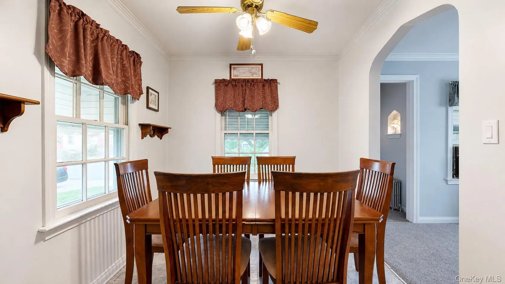 Dining area with white walls, multiple windows, a ceiling fan, and an arched doorway Dining area with white walls, multiple windows, a ceiling fan, and an arched doorway