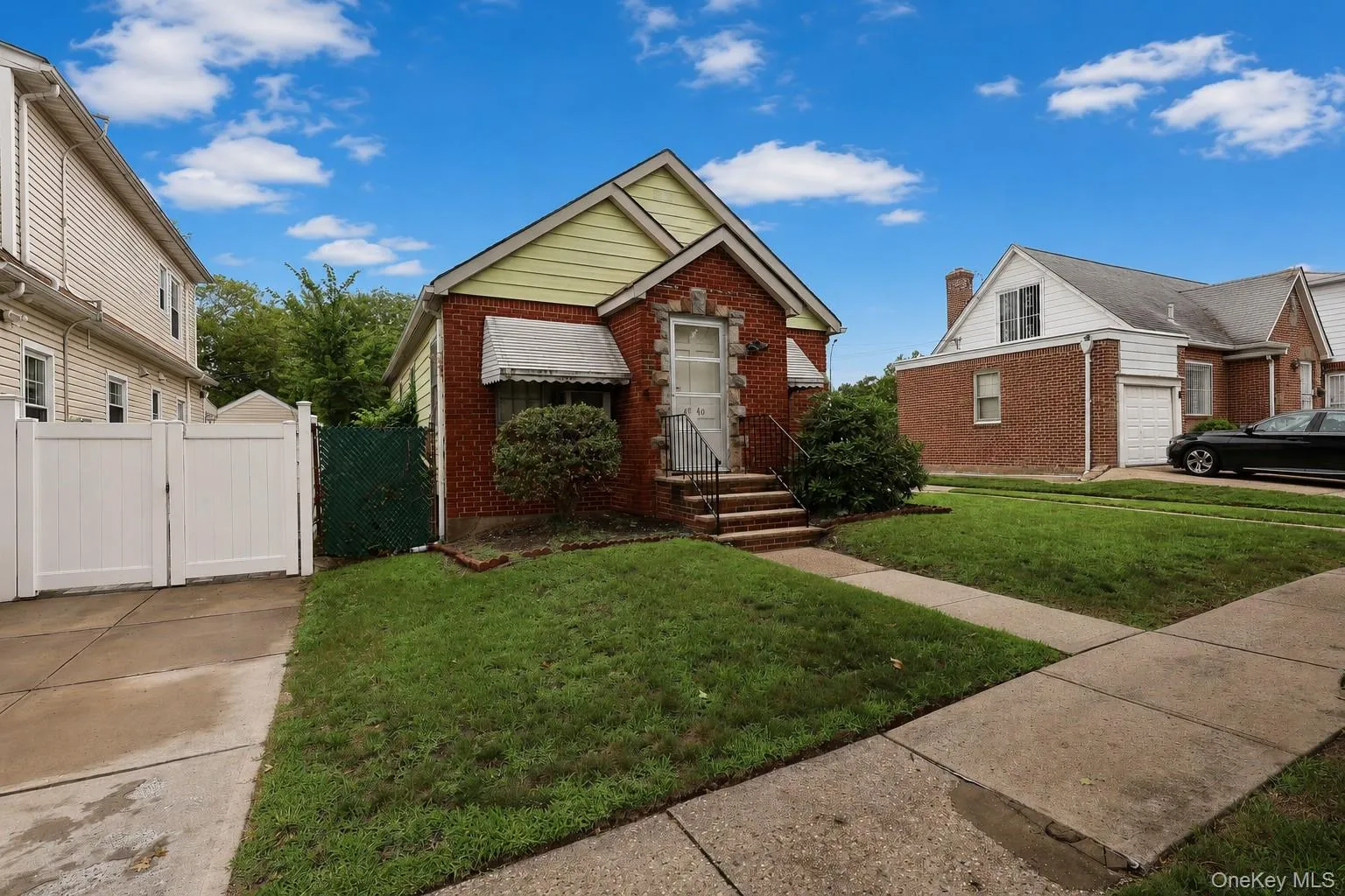 Brick and stone facade bungalow featuring a manicured front lawn, concrete walkway, and a private driveway with a white vinyl gate Brick and stone facade bungalow featuring a manicured front lawn, concrete walkway, and a private driveway with a white vinyl gate