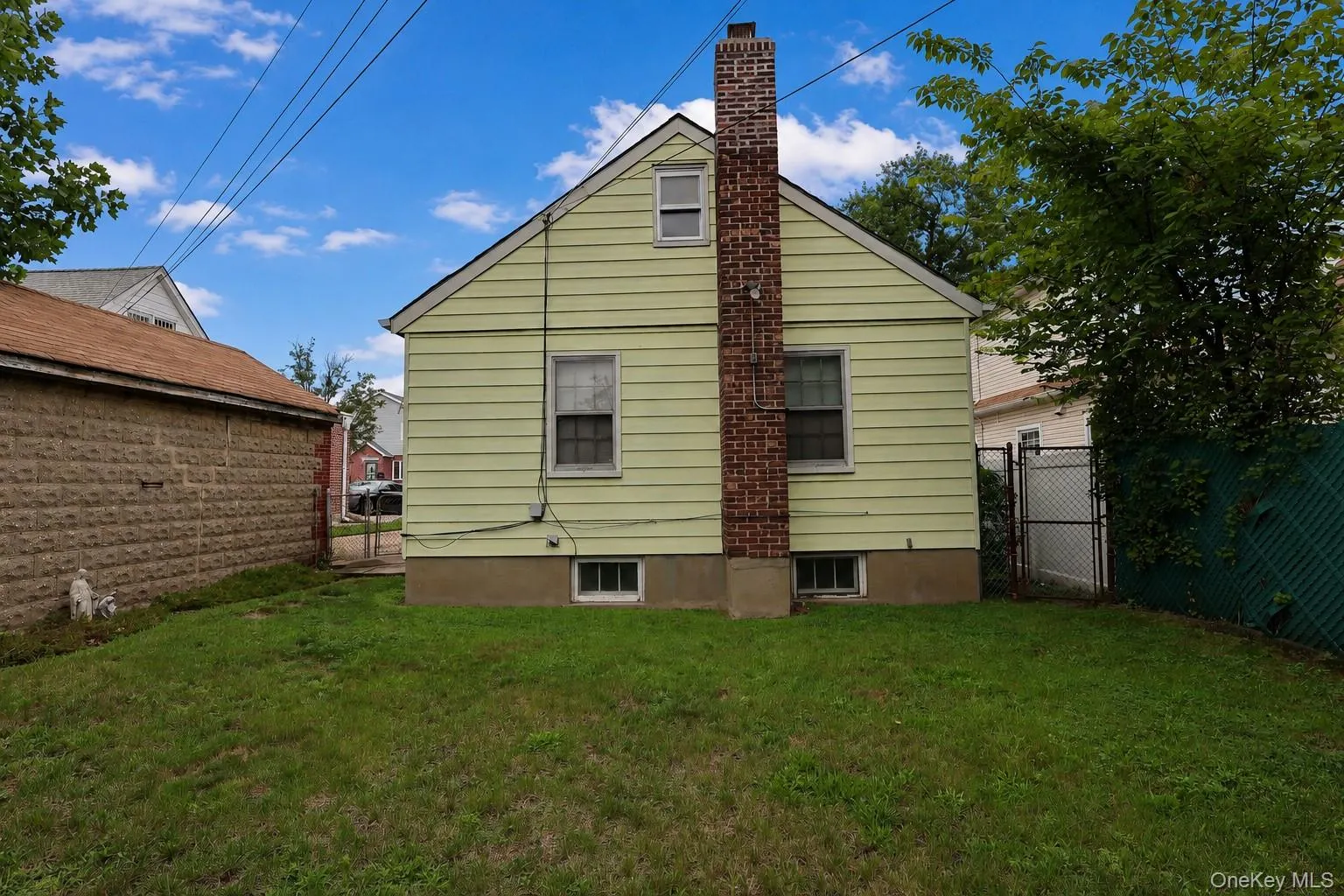 Rear exterior featuring light yellow siding, a brick chimney, and a small green lawn Rear exterior featuring light yellow siding, a brick chimney, and a small green lawn