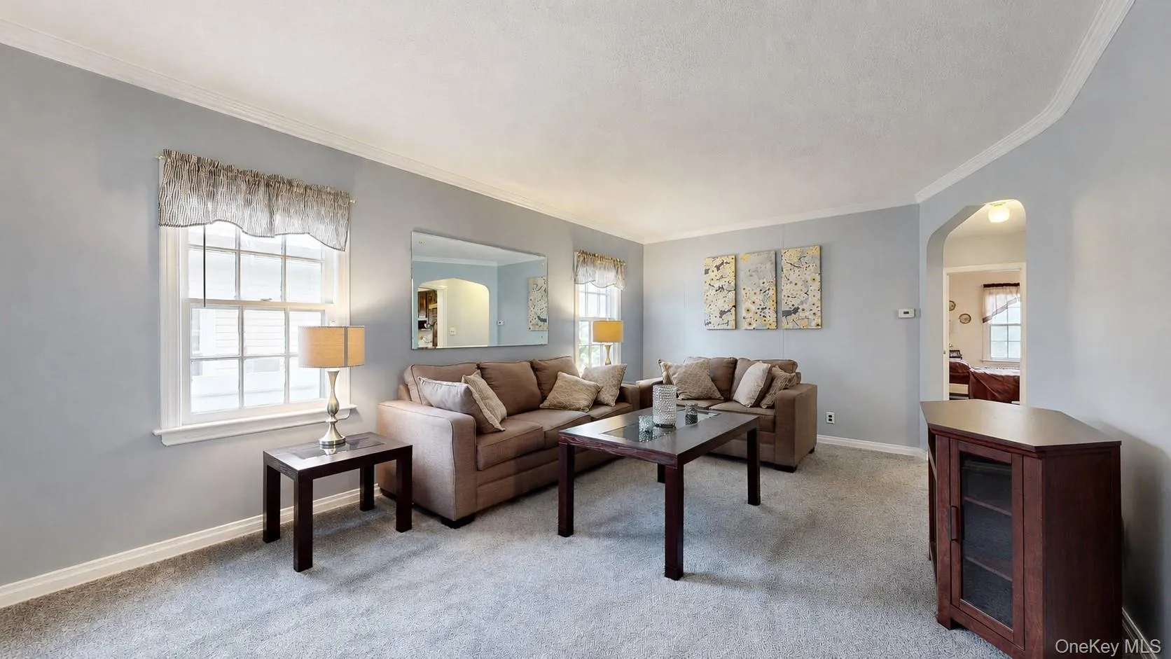 Spacious living area featuring light-colored wall paint, white crown molding, and light-colored carpet flooring Spacious living area featuring light-colored wall paint, white crown molding, and light-colored carpet flooring
