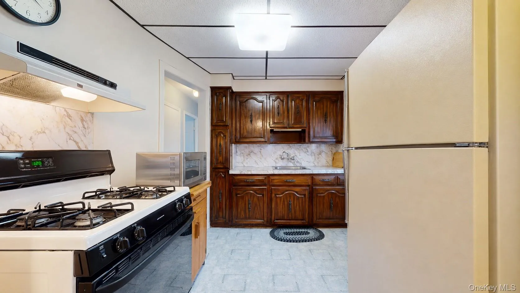 Kitchen featuring a white range with overhead ventilation, dark wood cabinetry, and light-toned mottled countertops Kitchen featuring a white range with overhead ventilation, dark wood cabinetry, and light-toned mottled countertops