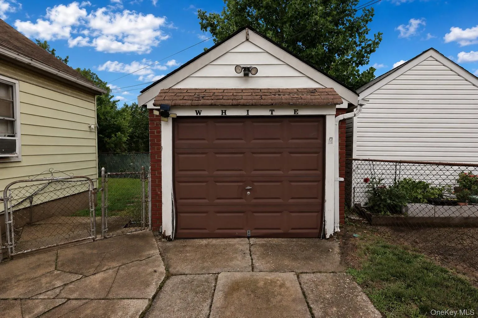 Detached garage featuring a brown panel door, white siding, and brick accents Detached garage featuring a brown panel door, white siding, and brick accents