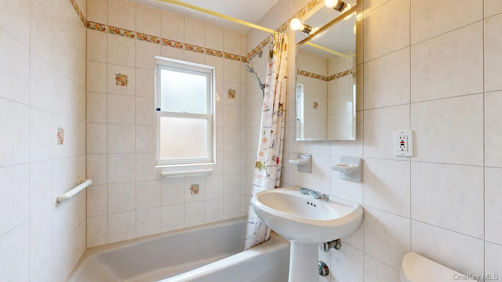 Full bathroom featuring a pedestal sink, a bathtub with a shower, and light-toned wall tiling Full bathroom featuring a pedestal sink, a bathtub with a shower, and light-toned wall tiling