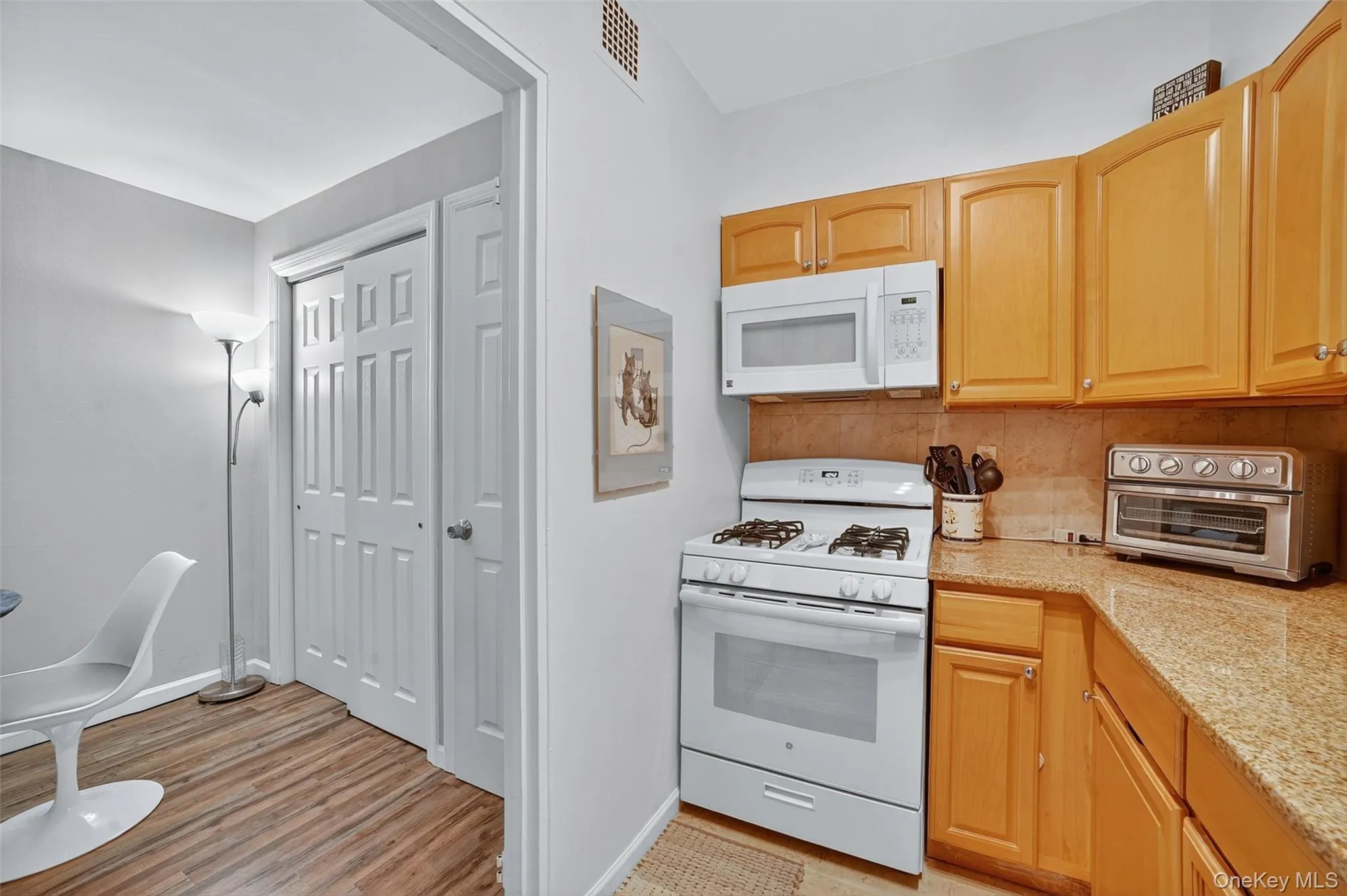 Kitchen with white appliances, light stone counters, tasteful backsplash, light wood-style floors, and light brown cabinetry Kitchen with white appliances, light stone counters, tasteful backsplash, light wood-style floors, and light brown cabinetry