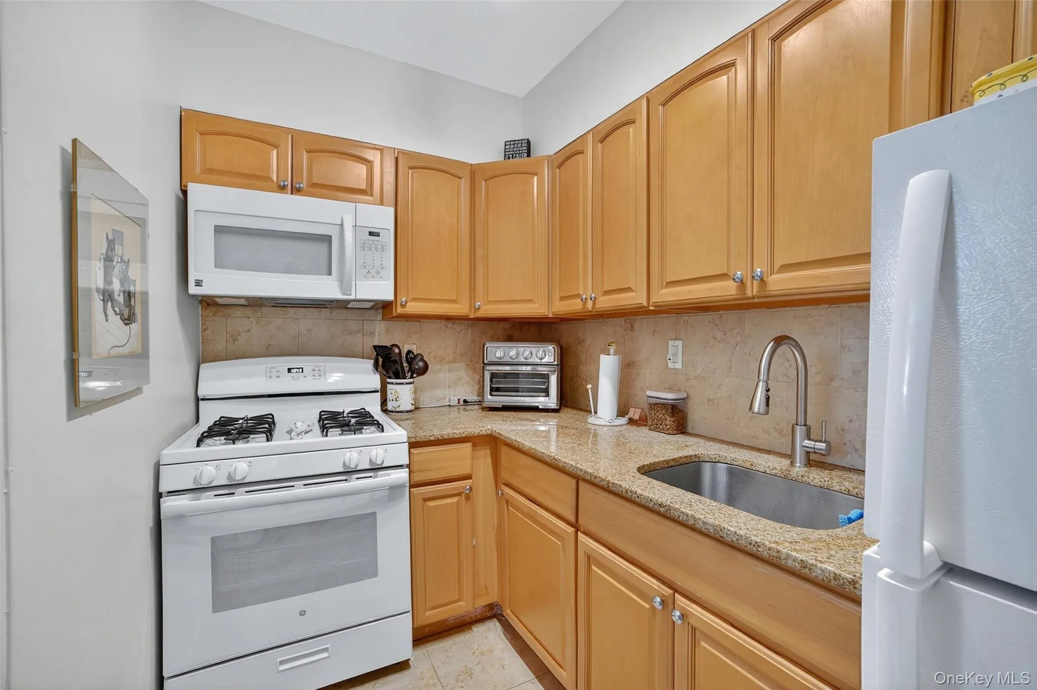 Kitchen featuring white appliances, tasteful backsplash, light stone countertops, and light brown cabinets Kitchen featuring white appliances, tasteful backsplash, light stone countertops, and light brown cabinets
