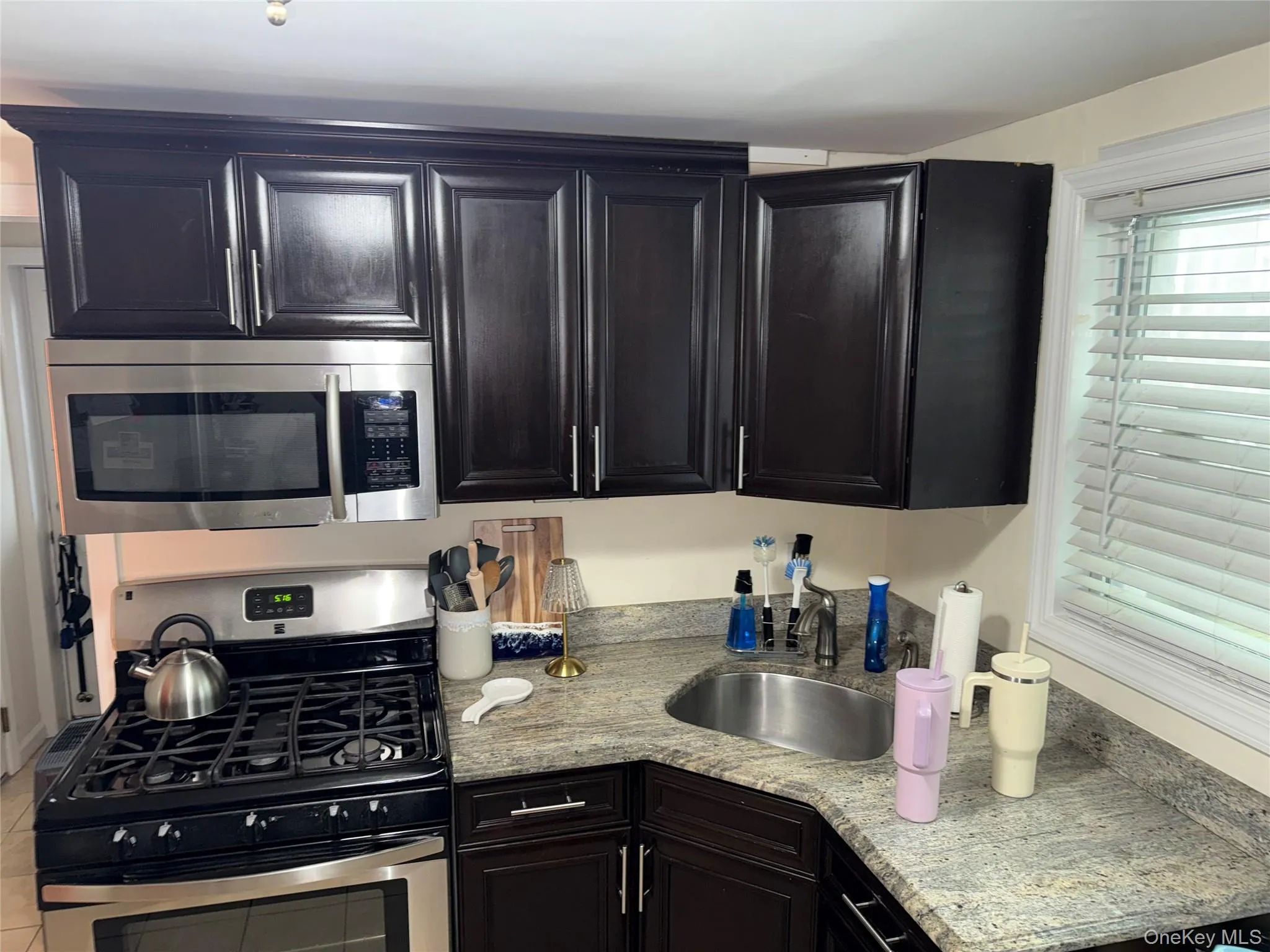 Kitchen with a sink, light stone countertops, dark cabinets, and appliances with stainless steel finishes Kitchen with a sink, light stone countertops, dark cabinets, and appliances with stainless steel finishes