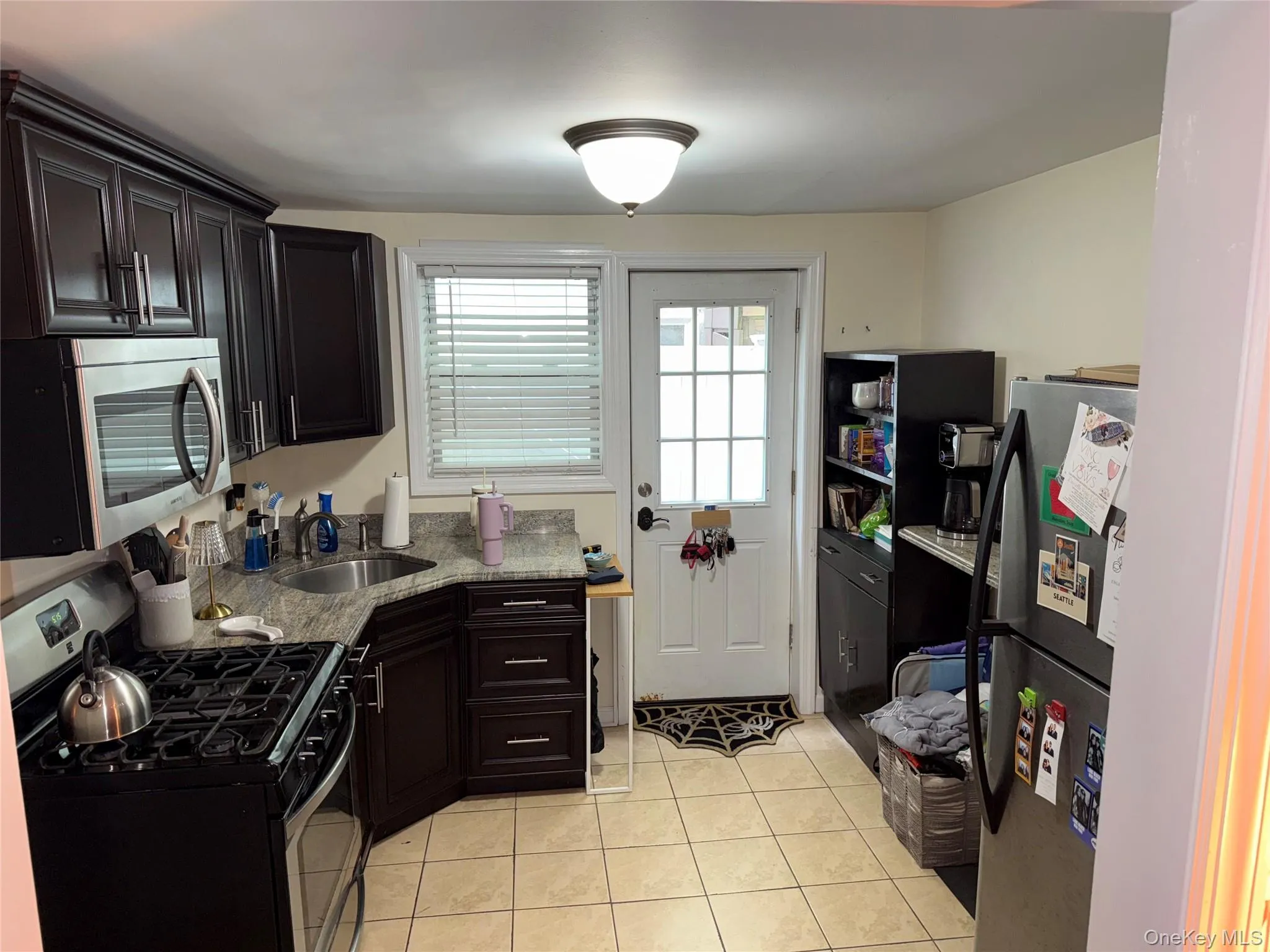 Kitchen featuring light tile patterned flooring, a sink, stainless steel appliances, and light stone counters Kitchen featuring light tile patterned flooring, a sink, stainless steel appliances, and light stone counters