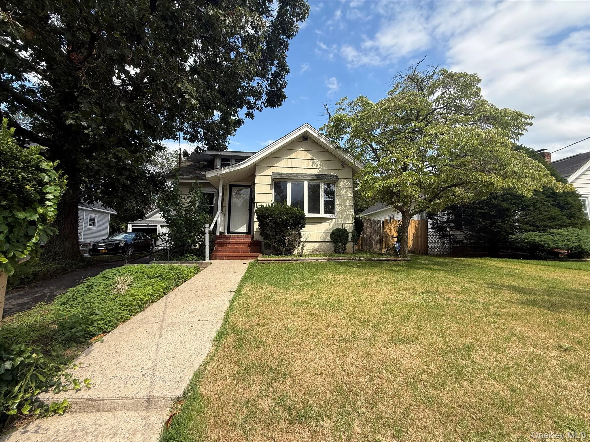 Single-story residence featuring a front yard, mature trees, concrete walkway, and brick porch steps Single-story residence featuring a front yard, mature trees, concrete walkway, and brick porch steps