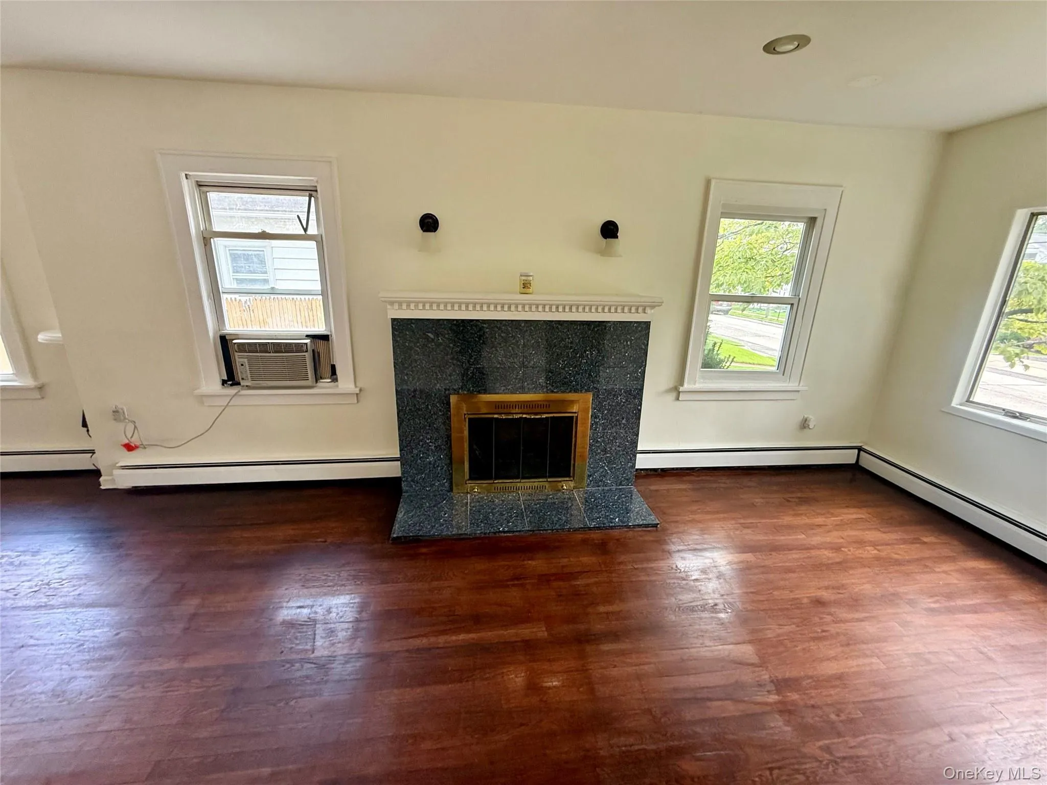 Living area featuring a fireplace with a dark stone surround and mantel, rich wood-finish flooring, and multiple windows Living area featuring a fireplace with a dark stone surround and mantel, rich wood-finish flooring, and multiple windows