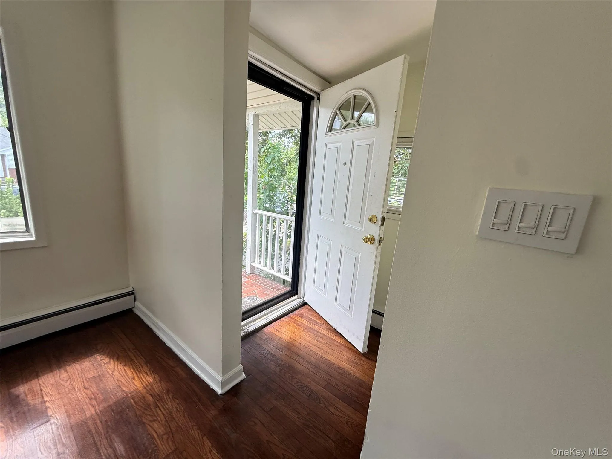 Foyer entry featuring a paneled door with an arched transom, wood-finish flooring, white baseboards, and a baseboard heating unit Foyer entry featuring a paneled door with an arched transom, wood-finish flooring, white baseboards, and a baseboard heating unit