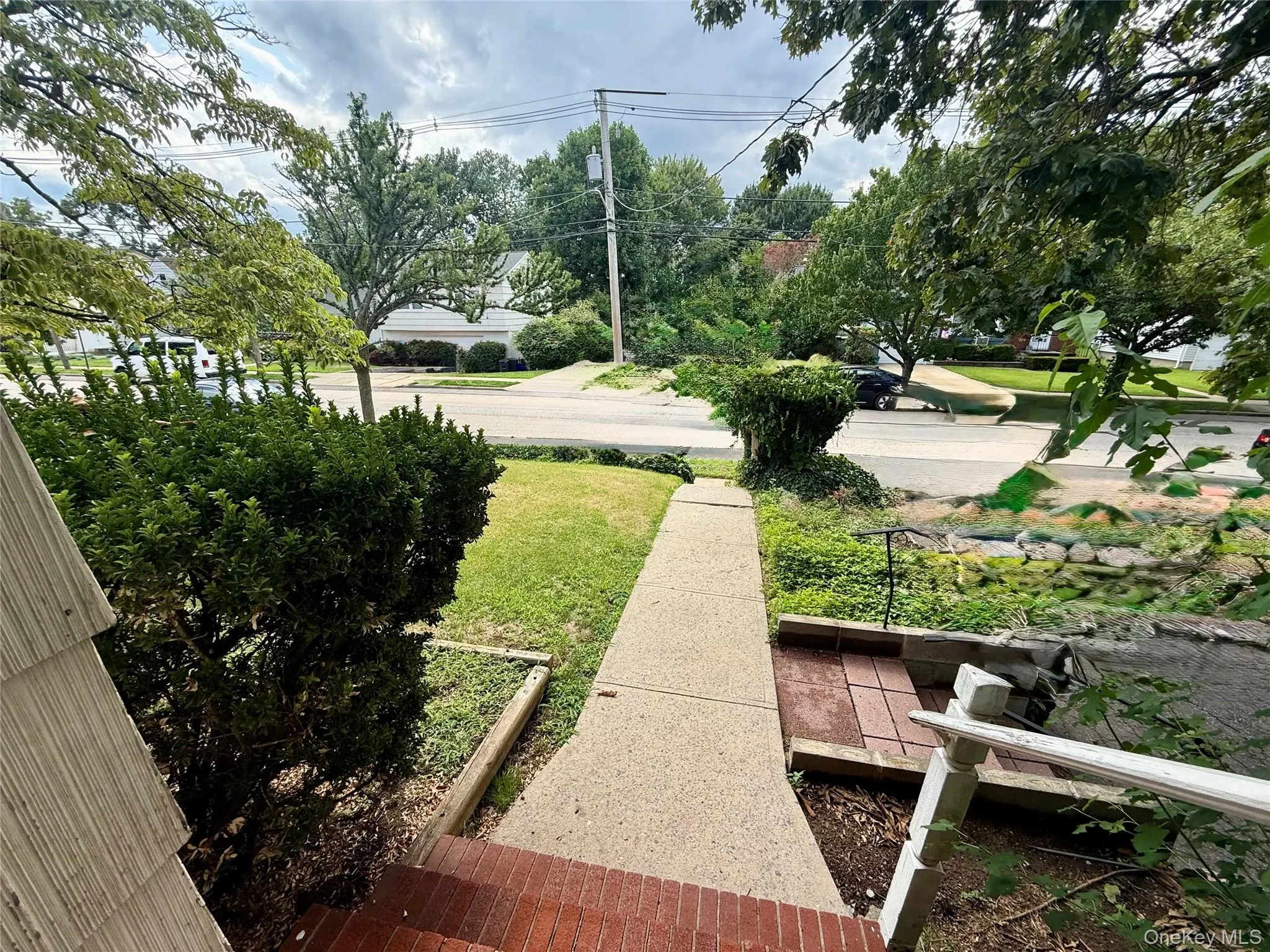Brick stairs leading to a concrete walkway, bordered by established green shrubs and a grassy lawn Brick stairs leading to a concrete walkway, bordered by established green shrubs and a grassy lawn