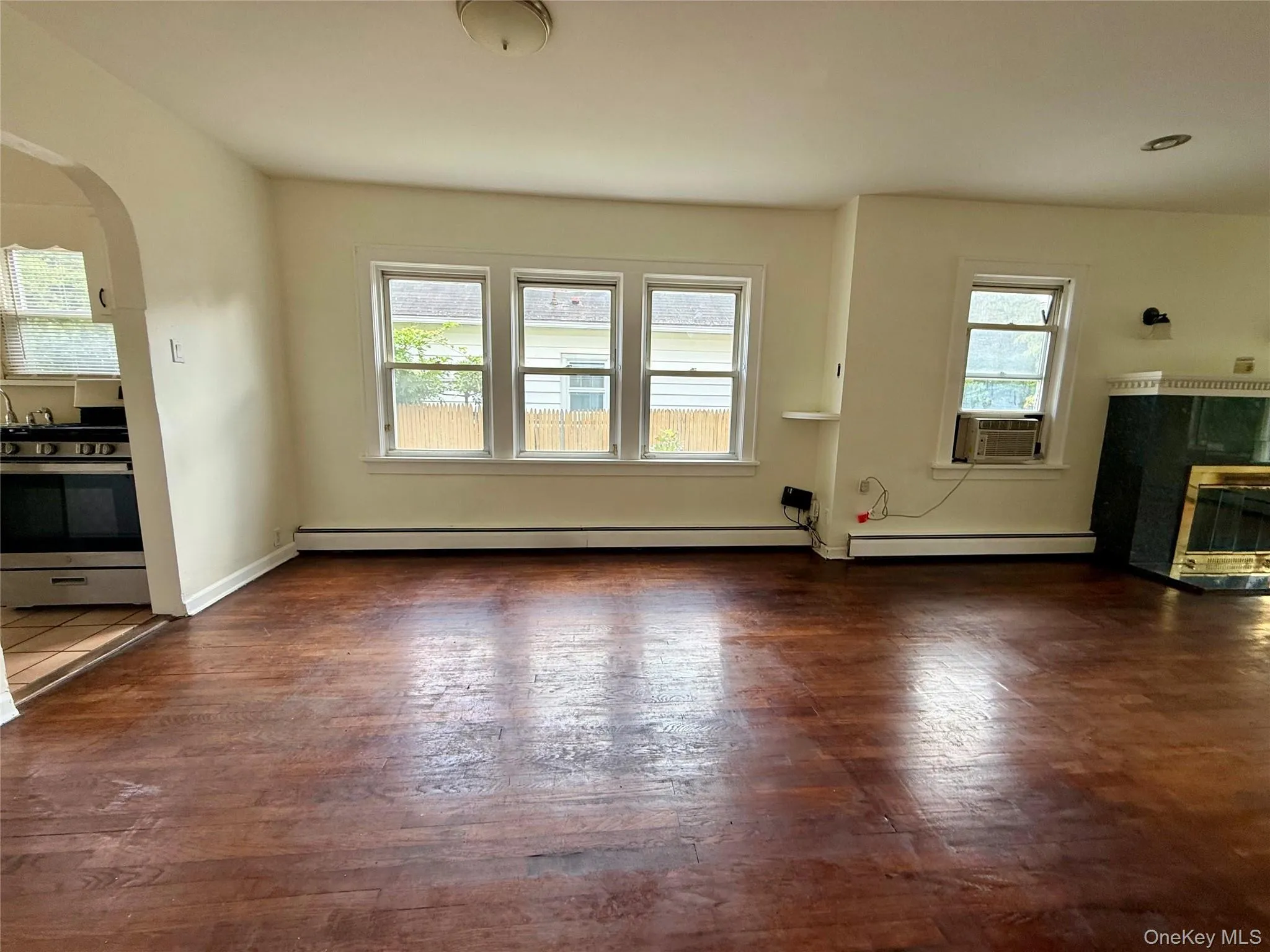 Spacious living area featuring wood-finish flooring, multiple windows, and an arched entry to the kitchen Spacious living area featuring wood-finish flooring, multiple windows, and an arched entry to the kitchen