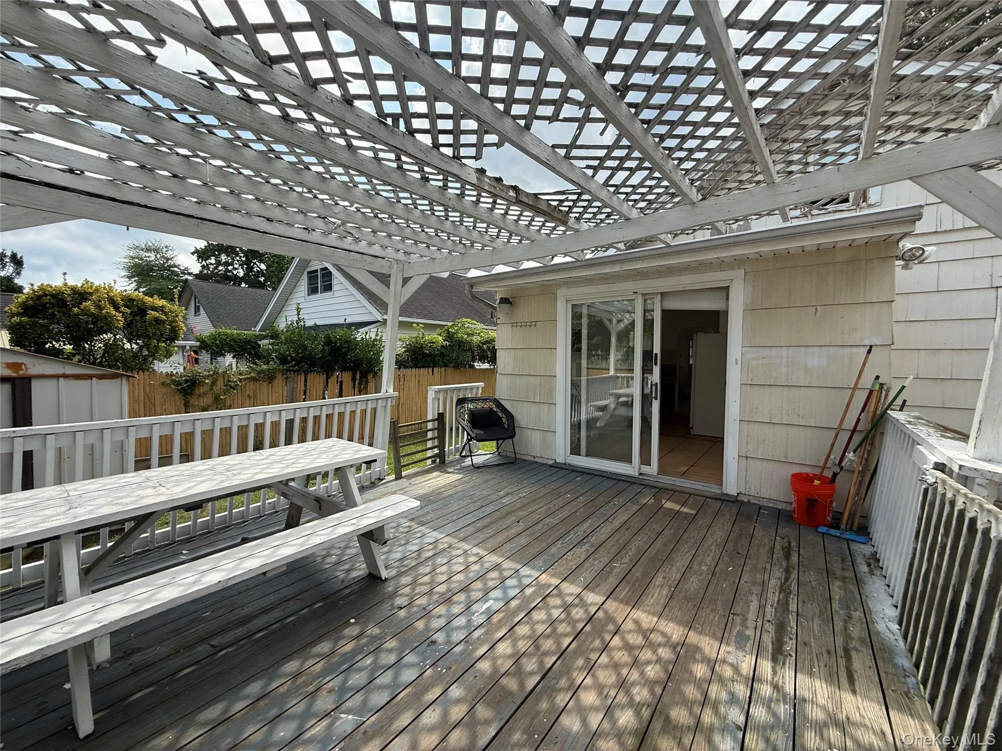 Outdoor deck featuring a white lattice pergola, sliding glass door access to the interior, wood-finish decking, and white painted railings Outdoor deck featuring a white lattice pergola, sliding glass door access to the interior, wood-finish decking, and white painted railings