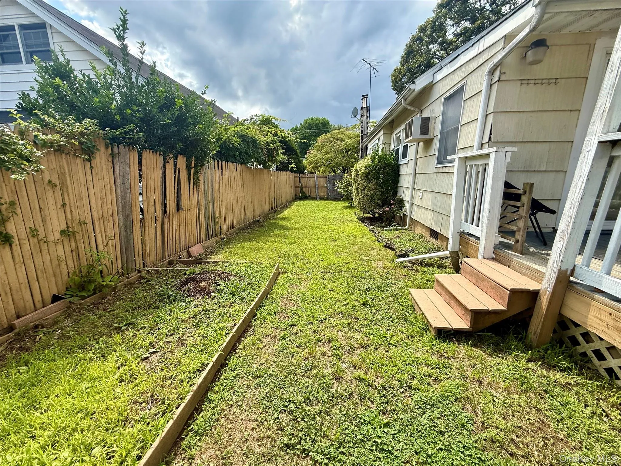 Spacious grass lawn featuring a wood plank fence, exterior siding, and exterior steps providing access to the property Spacious grass lawn featuring a wood plank fence, exterior siding, and exterior steps providing access to the property