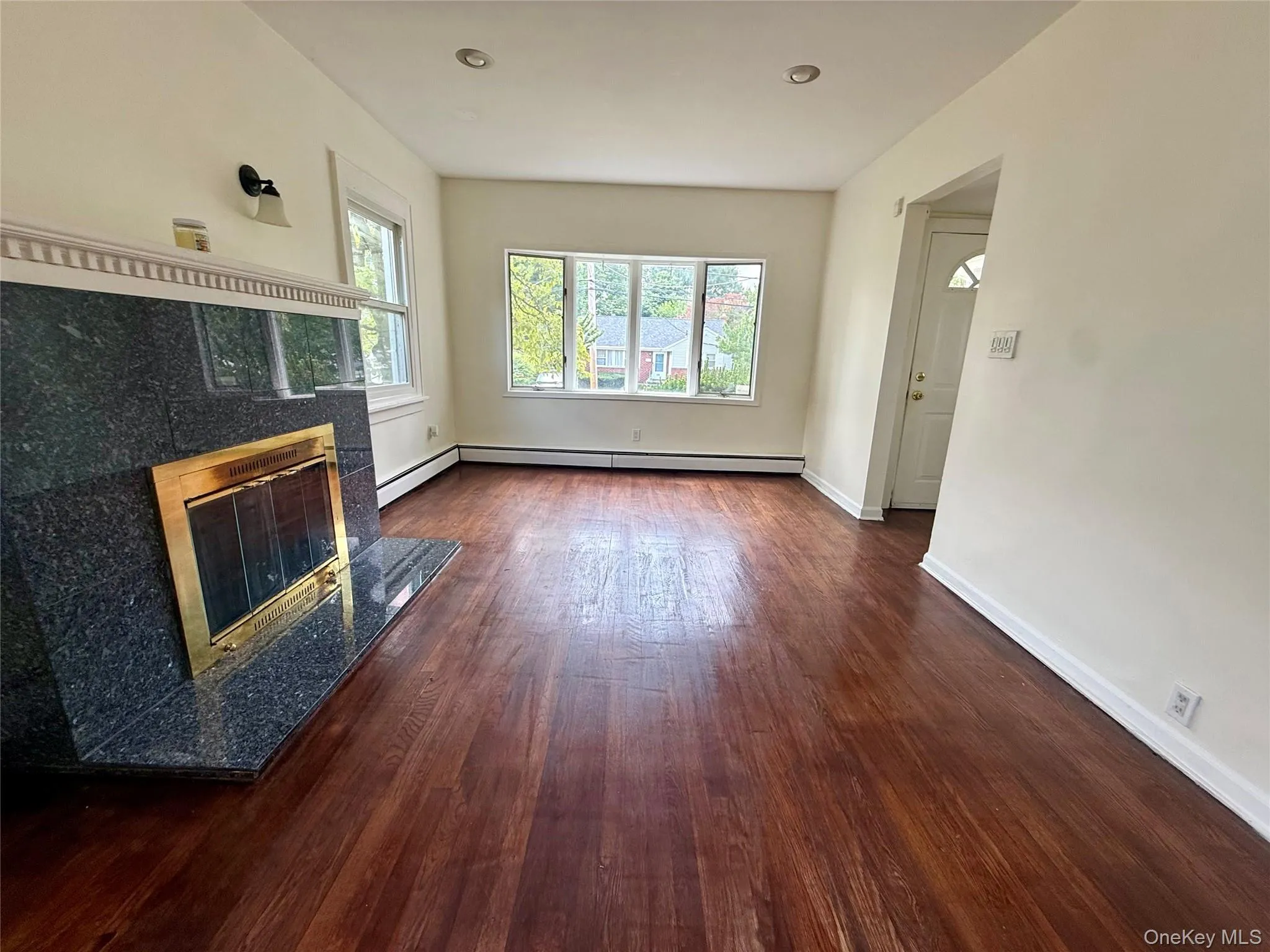 Spacious interior featuring wood-finish flooring and a fireplace with a dark stone surround and hearth Spacious interior featuring wood-finish flooring and a fireplace with a dark stone surround and hearth