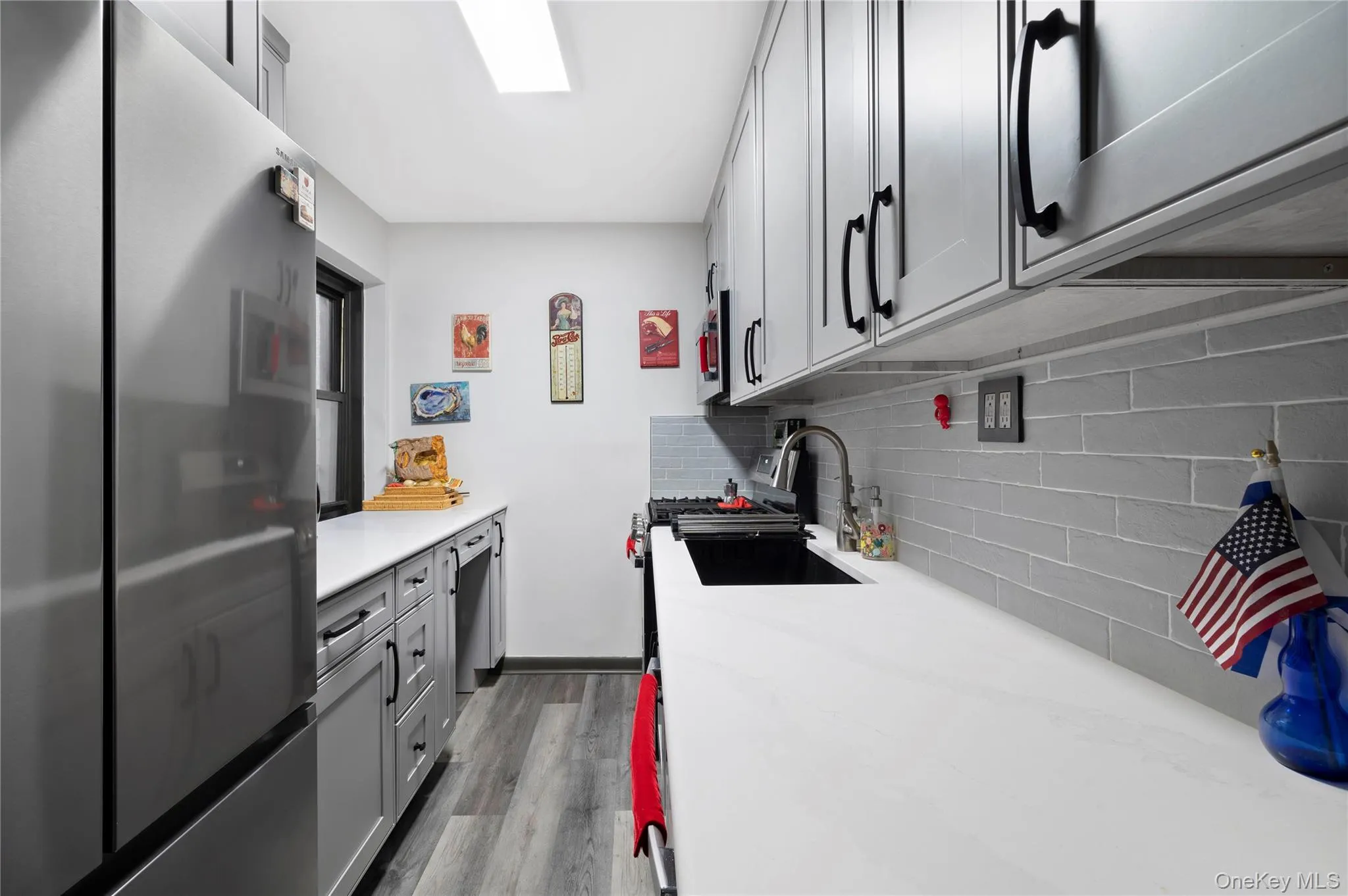 Galley kitchen featuring gray shaker-style cabinetry with matte black hardware, white countertops, and a gray subway tile backsplash Galley kitchen featuring gray shaker-style cabinetry with matte black hardware, white countertops, and a gray subway tile backsplash