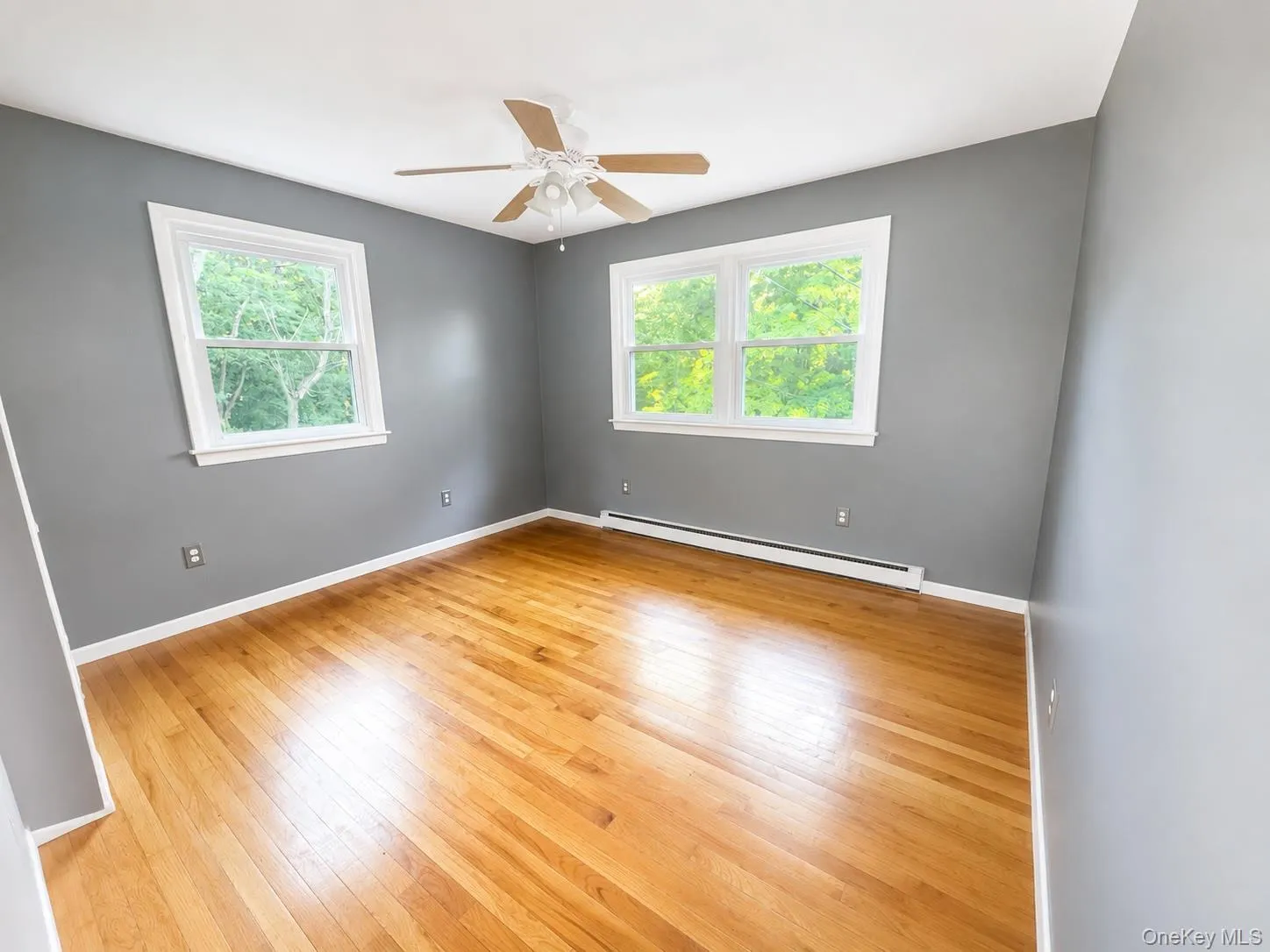Bright interior space featuring wood-finish flooring, white trim, and two large windows with white frames Bright interior space featuring wood-finish flooring, white trim, and two large windows with white frames