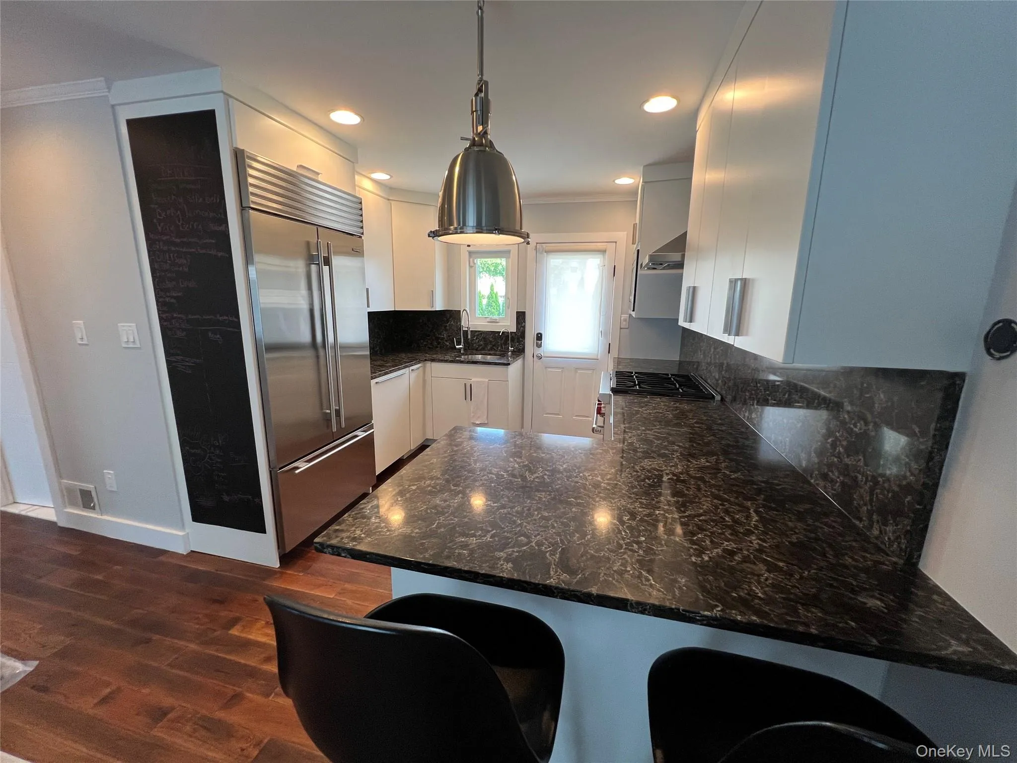 Sleek, modern kitchen featuring stainless steel appliances, white cabinetry, and a spacious granite-look countertop island with seating for two Sleek, modern kitchen featuring stainless steel appliances, white cabinetry, and a spacious granite-look countertop island with seating for two
