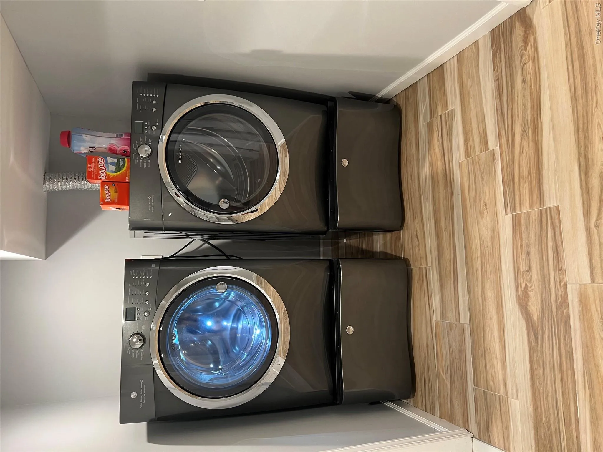 Dedicated laundry room featuring side-by-side front-load washers and dryers with pedestal bases, ample countertop storage above, wood-finish flooring, and recessed ceiling lighting for optimal functionality Dedicated laundry room featuring side-by-side front-load washers and dryers with pedestal bases, ample countertop storage above, wood-finish flooring, and recessed ceiling lighting for optimal functionality