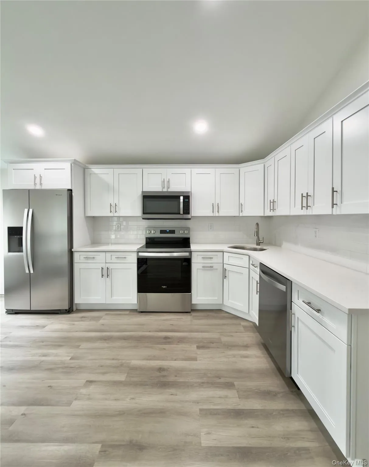 White cabinetry with brushed nickel hardware, stainless steel appliances, light-toned countertops, subway tile backsplash. White cabinetry with brushed nickel hardware, stainless steel appliances, light-toned countertops, subway tile backsplash.