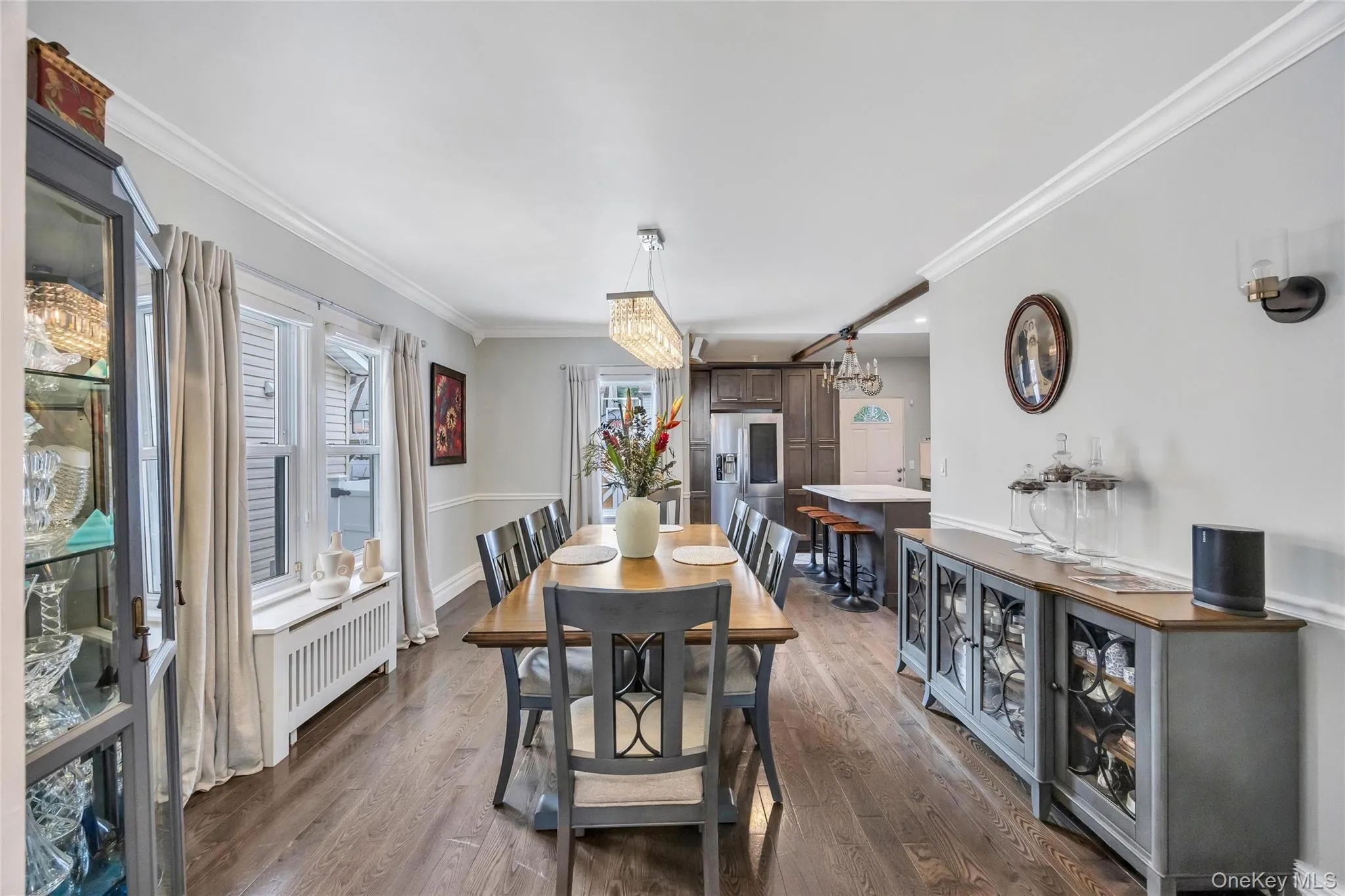 Spacious dining area featuring wood-finish flooring, white crown molding, and a contemporary linear chandelier Spacious dining area featuring wood-finish flooring, white crown molding, and a contemporary linear chandelier