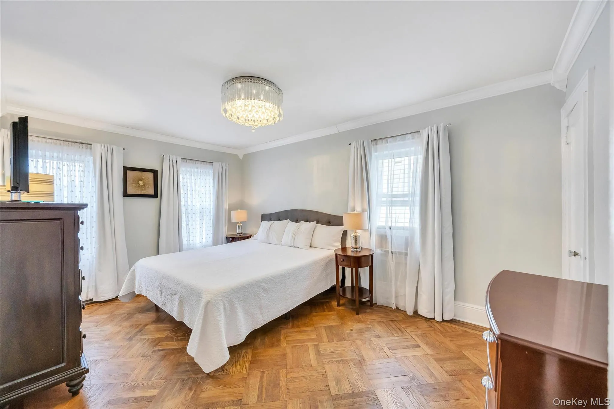 Bright room featuring wood-finish parquet flooring, crown molding, and a crystal chandelier Bright room featuring wood-finish parquet flooring, crown molding, and a crystal chandelier