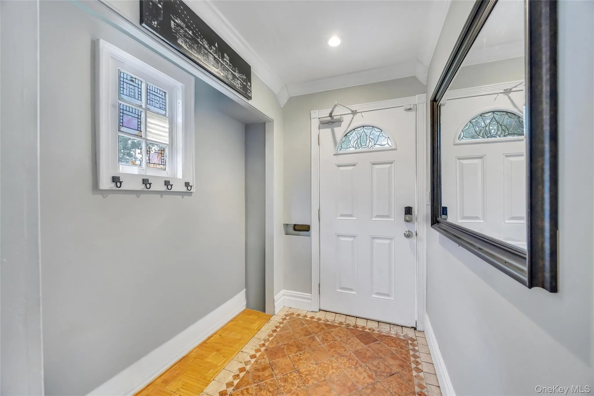 Entryway featuring a white paneled door with an arched decorative glass insert, complemented by a large framed mirror Entryway featuring a white paneled door with an arched decorative glass insert, complemented by a large framed mirror