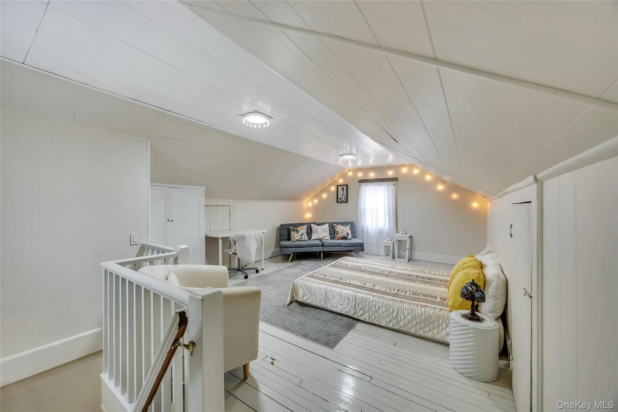 Spacious attic conversion featuring white wood-finish flooring, a pitched ceiling with exposed beams, and built-in storage solutions Spacious attic conversion featuring white wood-finish flooring, a pitched ceiling with exposed beams, and built-in storage solutions