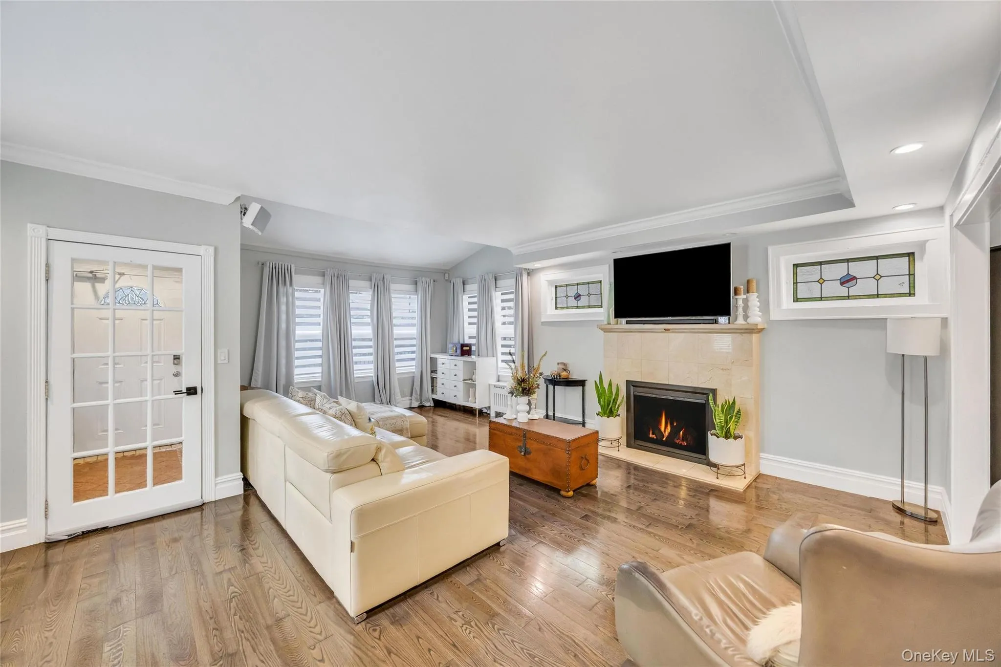 Living area featuring wood-finish flooring, a fireplace with a stone surround, recessed lighting, crown molding, and multiple windows with blinds Living area featuring wood-finish flooring, a fireplace with a stone surround, recessed lighting, crown molding, and multiple windows with blinds