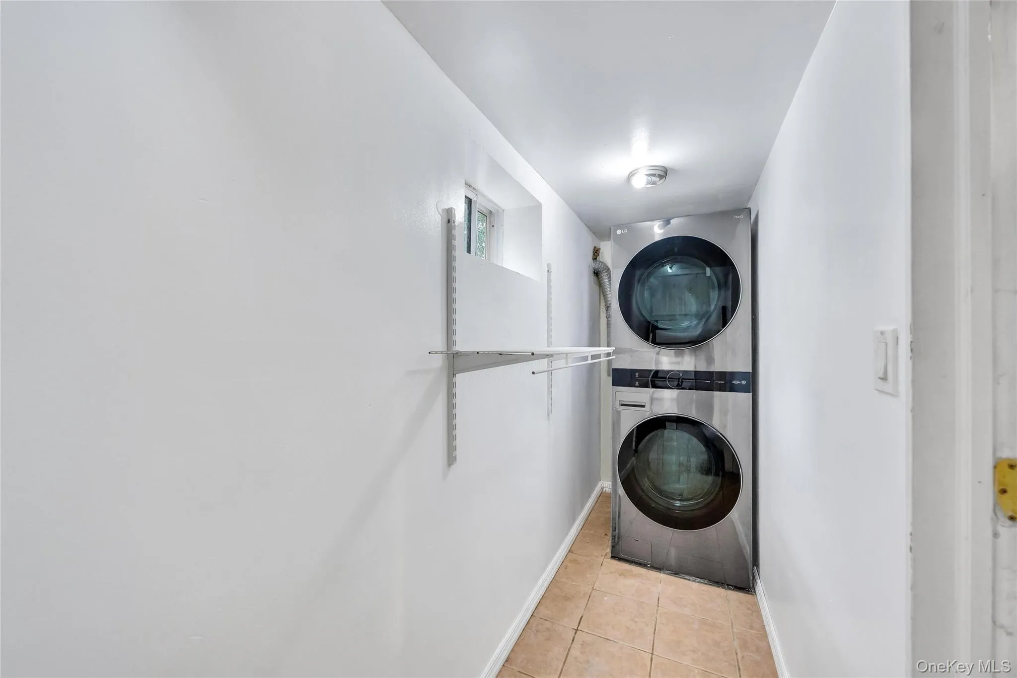 Dedicated laundry area featuring a stacked washer and dryer unit, tiled flooring, and an overhead light fixture Dedicated laundry area featuring a stacked washer and dryer unit, tiled flooring, and an overhead light fixture