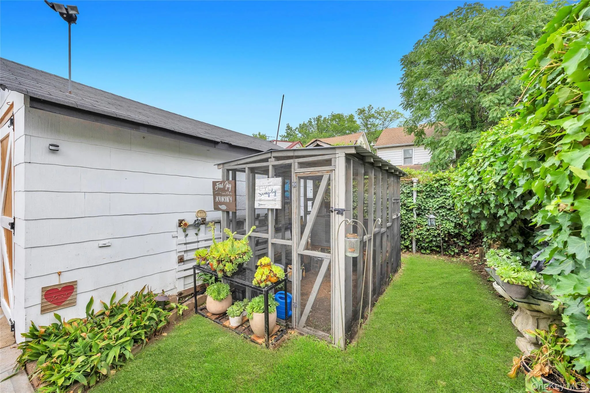 Side yard featuring a screened enclosure, lush green lawn, mature perimeter plantings, and a dedicated garden area Side yard featuring a screened enclosure, lush green lawn, mature perimeter plantings, and a dedicated garden area