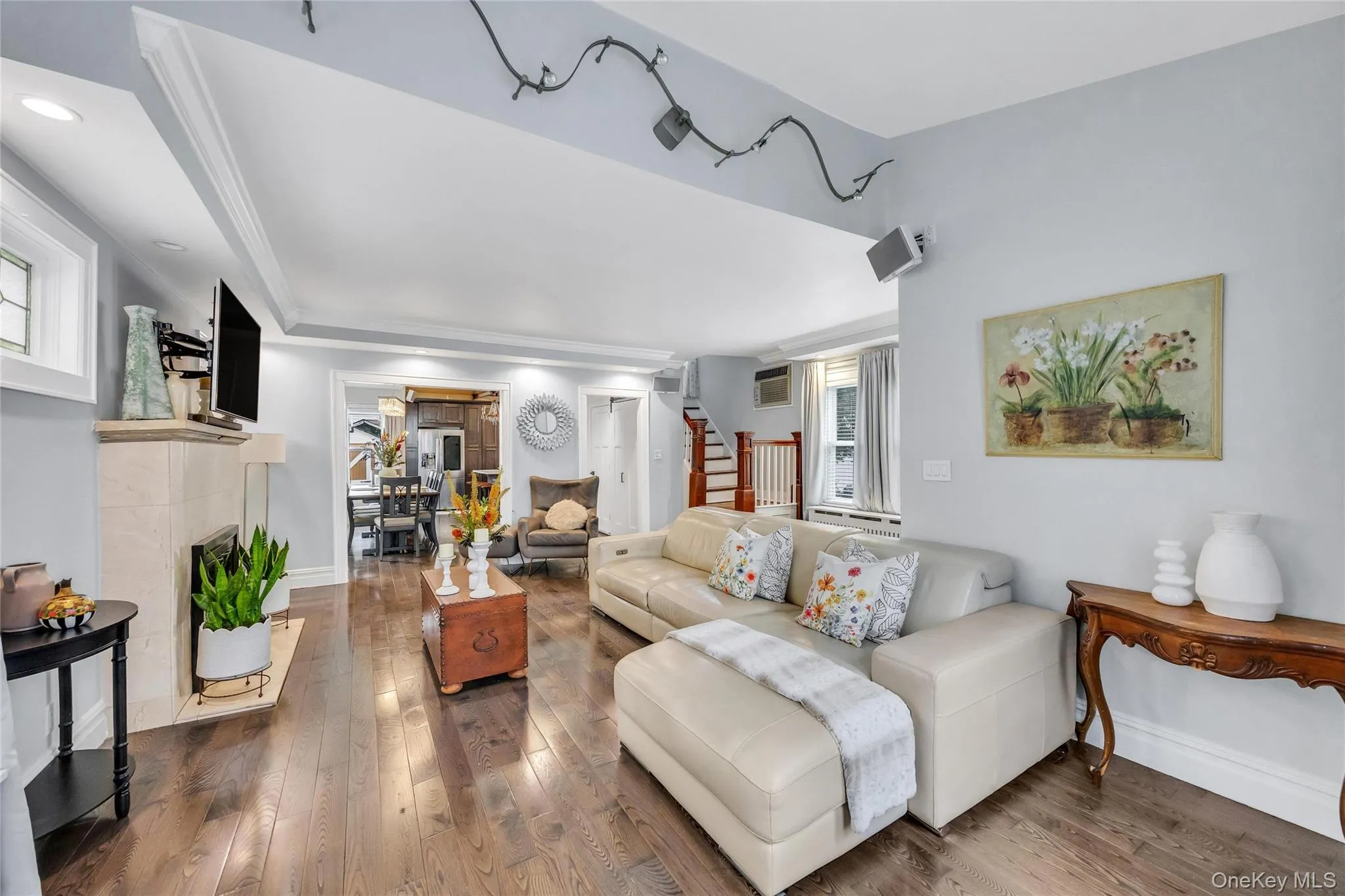Living area featuring dark wood-finish flooring, a fireplace with a light-toned stone surround, recessed lighting, and crown molding Living area featuring dark wood-finish flooring, a fireplace with a light-toned stone surround, recessed lighting, and crown molding