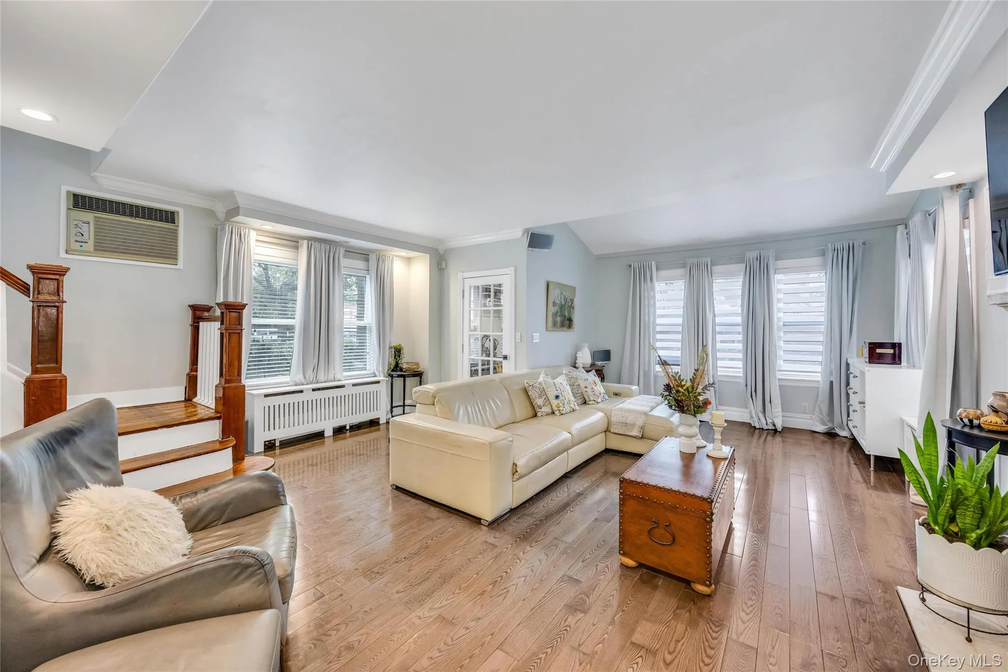 Spacious living area featuring wood-finish flooring, a bay window with blinds, and white crown molding Spacious living area featuring wood-finish flooring, a bay window with blinds, and white crown molding