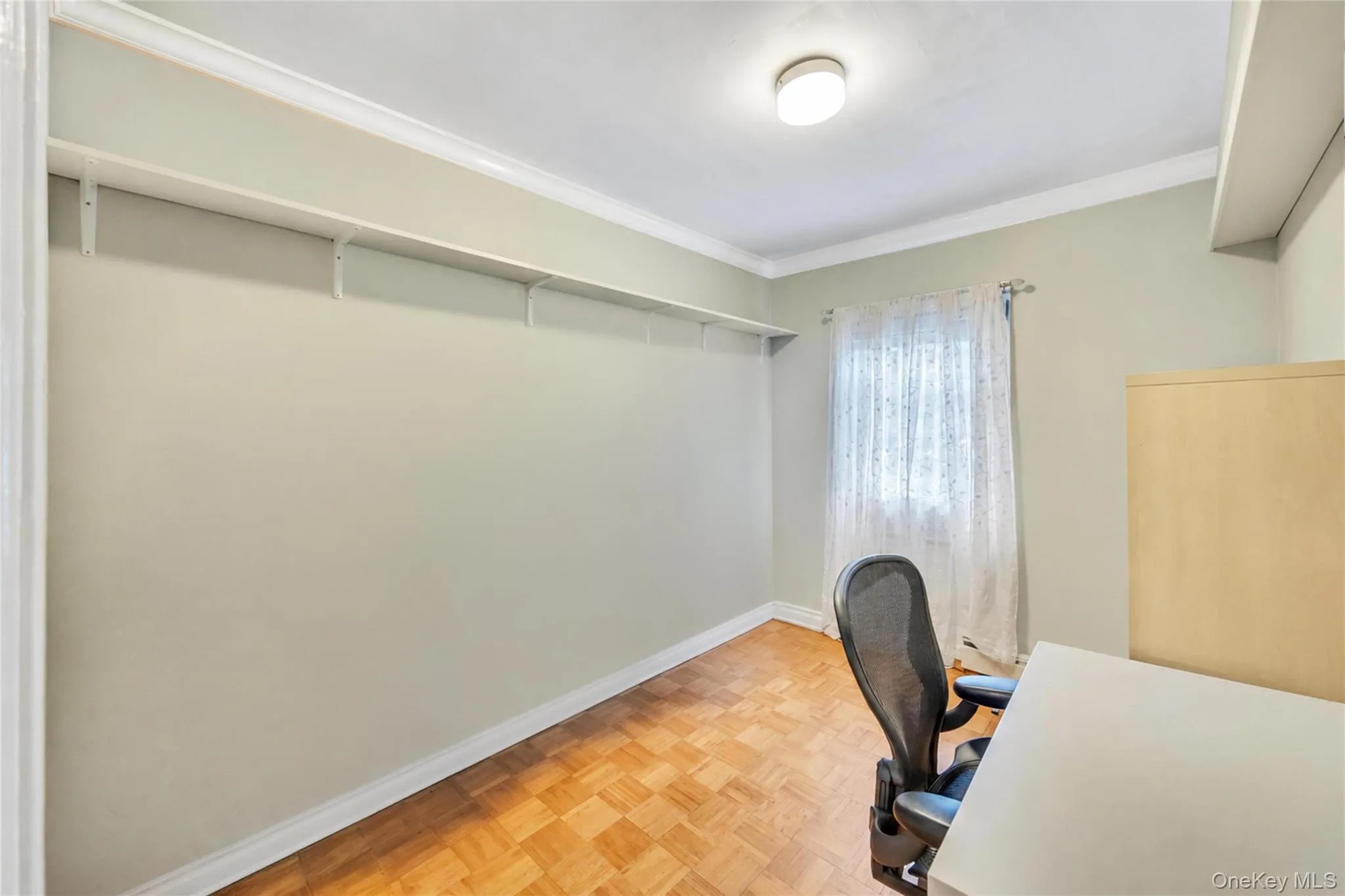 Room featuring wood-finish parquet flooring, crown molding, and a built-in wall shelf Room featuring wood-finish parquet flooring, crown molding, and a built-in wall shelf