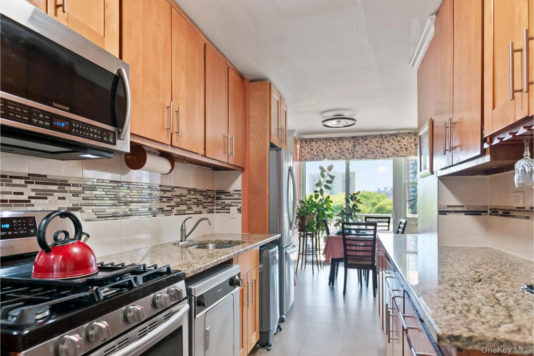Galley kitchen featuring light wood cabinetry, stone countertops, a stainless steel gas range, and a mosaic tile backsplash Galley kitchen featuring light wood cabinetry, stone countertops, a stainless steel gas range, and a mosaic tile backsplash