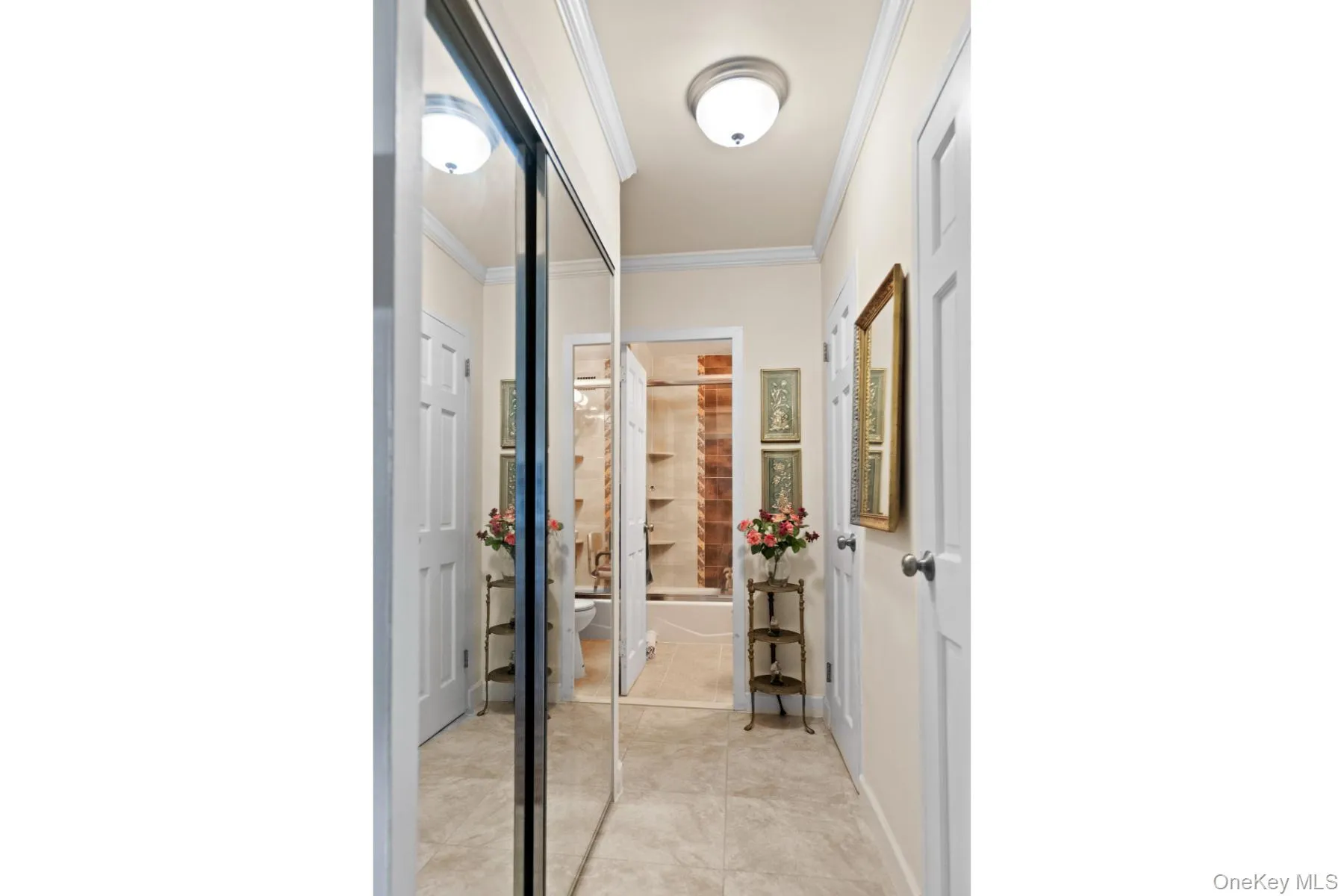 Hallway featuring mirrored sliding closet doors, crown molding, a flush mount ceiling light, and light-colored tile flooring Hallway featuring mirrored sliding closet doors, crown molding, a flush mount ceiling light, and light-colored tile flooring
