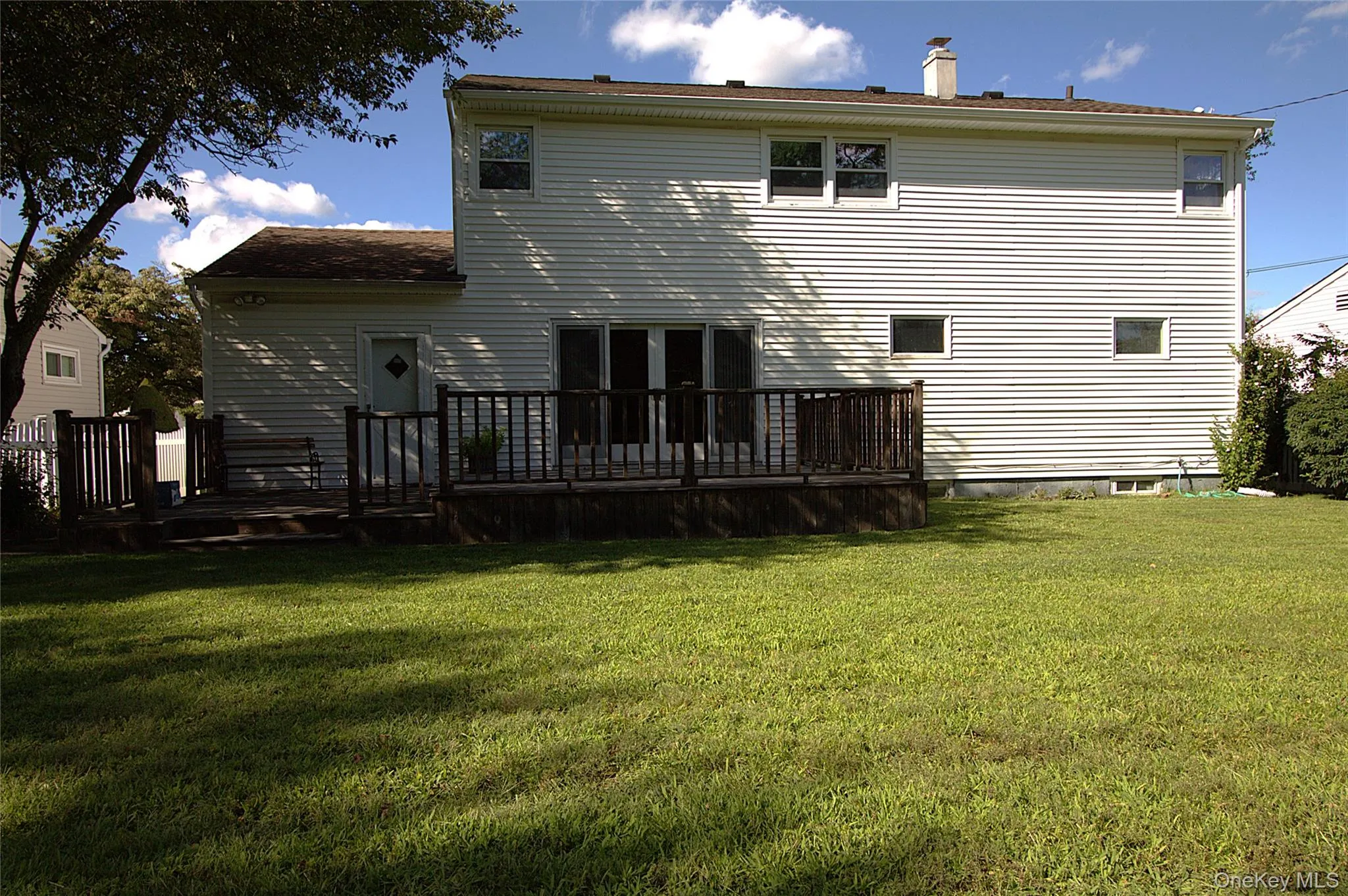 Expansive yard featuring a large wooden deck with railing, white siding, and multiple windows Expansive yard featuring a large wooden deck with railing, white siding, and multiple windows
