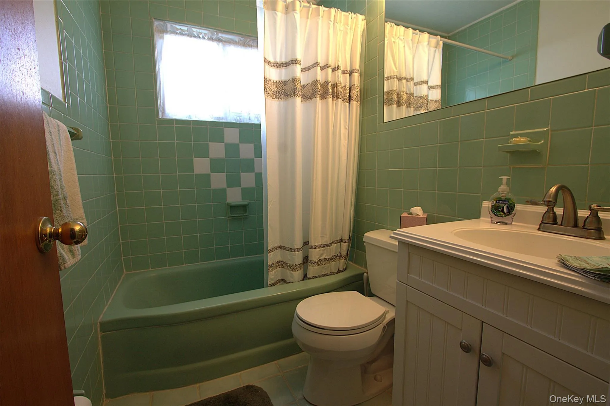 Green tiled walls with accent pattern, green bathtub, white vanity with integrated sink, and wall-mounted mirror Green tiled walls with accent pattern, green bathtub, white vanity with integrated sink, and wall-mounted mirror