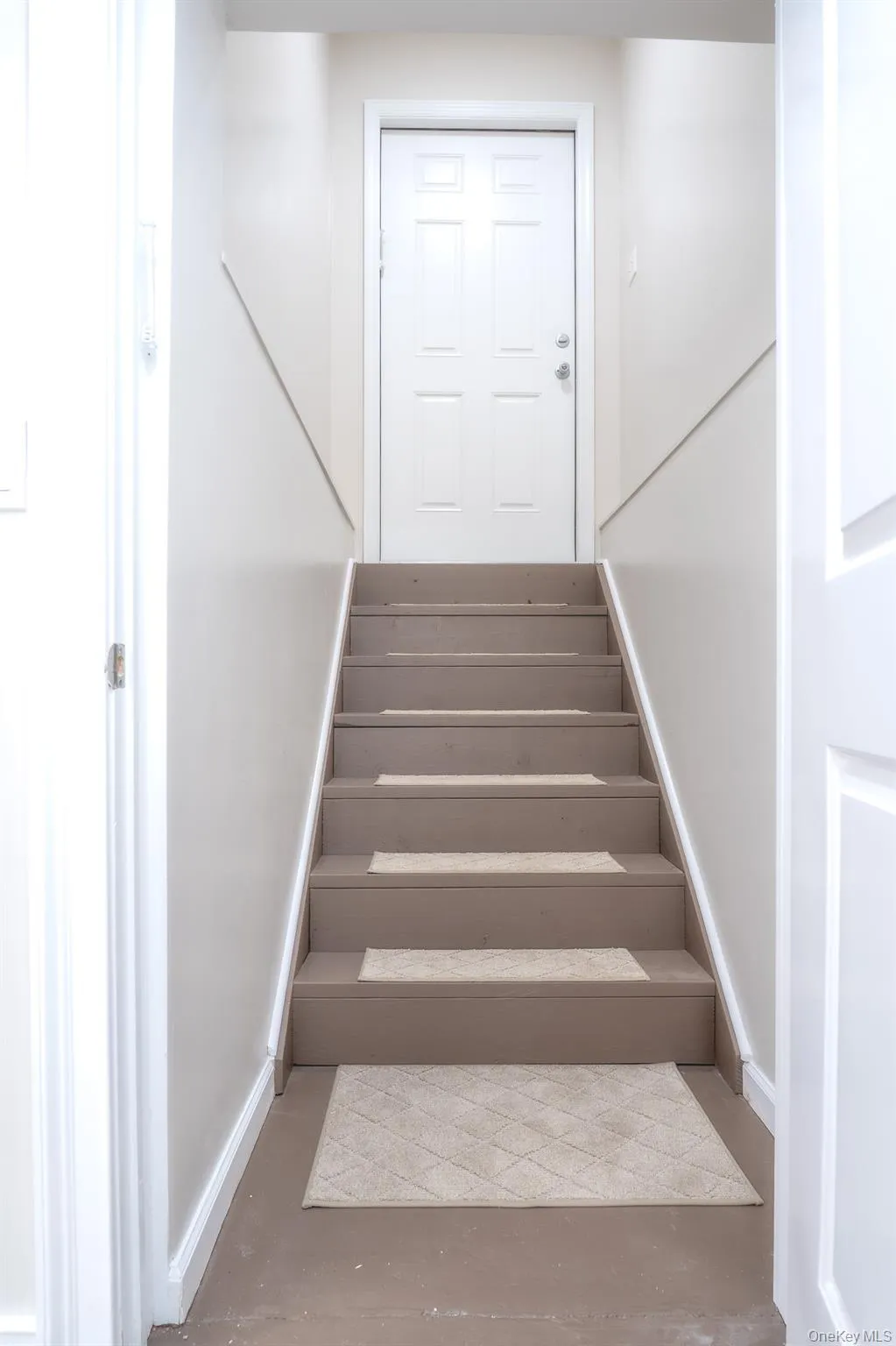 Interior staircase with painted treads and risers, featuring a paneled door with hardware at the top landing Interior staircase with painted treads and risers, featuring a paneled door with hardware at the top landing
