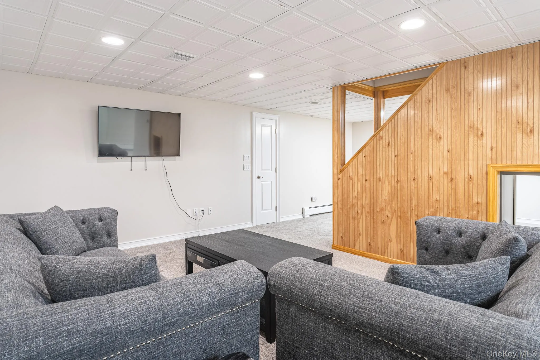 Modern recreational space featuring multiple upholstered seating areas with nailhead trim detailing, flat-screen television mounted on accent wall, and distinctive wood-paneled architectural feature Modern recreational space featuring multiple upholstered seating areas with nailhead trim detailing, flat-screen television mounted on accent wall, and distinctive wood-paneled architectural feature