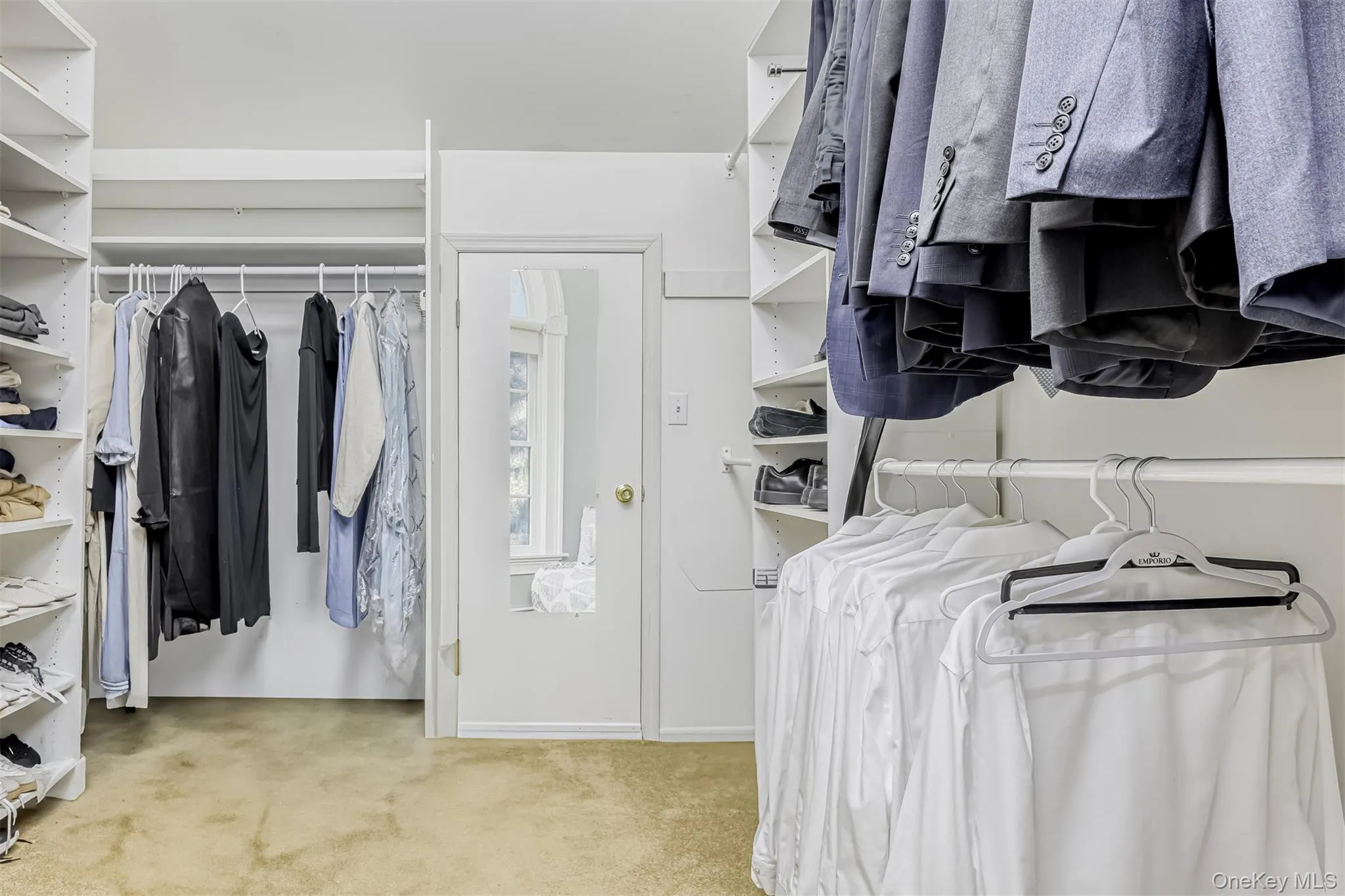Spacious walk-in closet featuring extensive built-in shelving and hanging rods, neutral finishes, and abundant natural light from transom windows Spacious walk-in closet featuring extensive built-in shelving and hanging rods, neutral finishes, and abundant natural light from transom windows