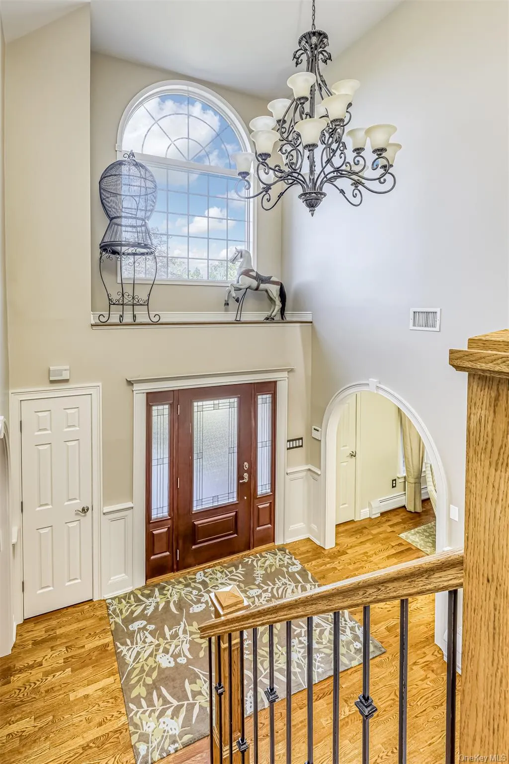 Two-story foyer featuring a grand arched window, an ornate chandelier, and hardwood flooring Two-story foyer featuring a grand arched window, an ornate chandelier, and hardwood flooring