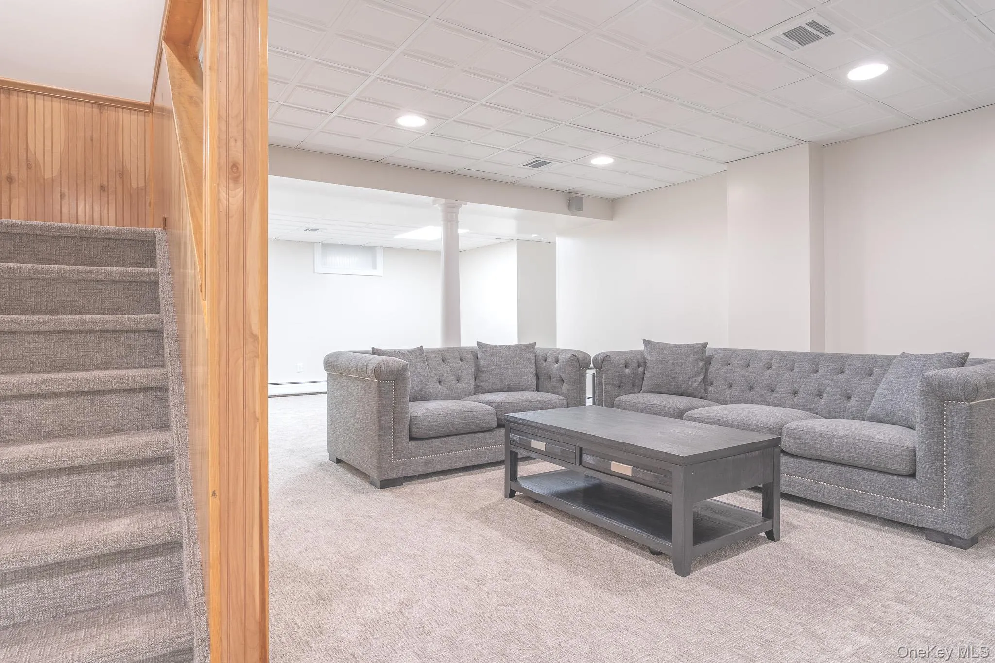 Spacious finished basement featuring a generous L-shaped sectional configuration area, neutral carpet flooring, recessed ceiling lighting, and a low-profile coffee table Spacious finished basement featuring a generous L-shaped sectional configuration area, neutral carpet flooring, recessed ceiling lighting, and a low-profile coffee table