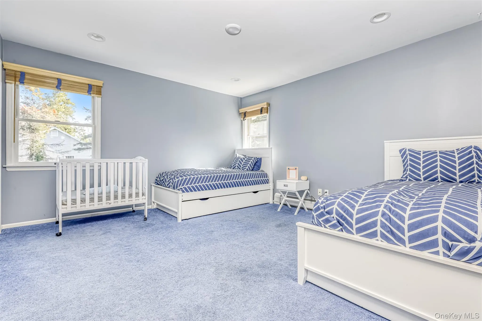 Spacious room featuring light blue carpeting, two windows with wood-finish blinds, recessed lighting, and light blue wall tones Spacious room featuring light blue carpeting, two windows with wood-finish blinds, recessed lighting, and light blue wall tones