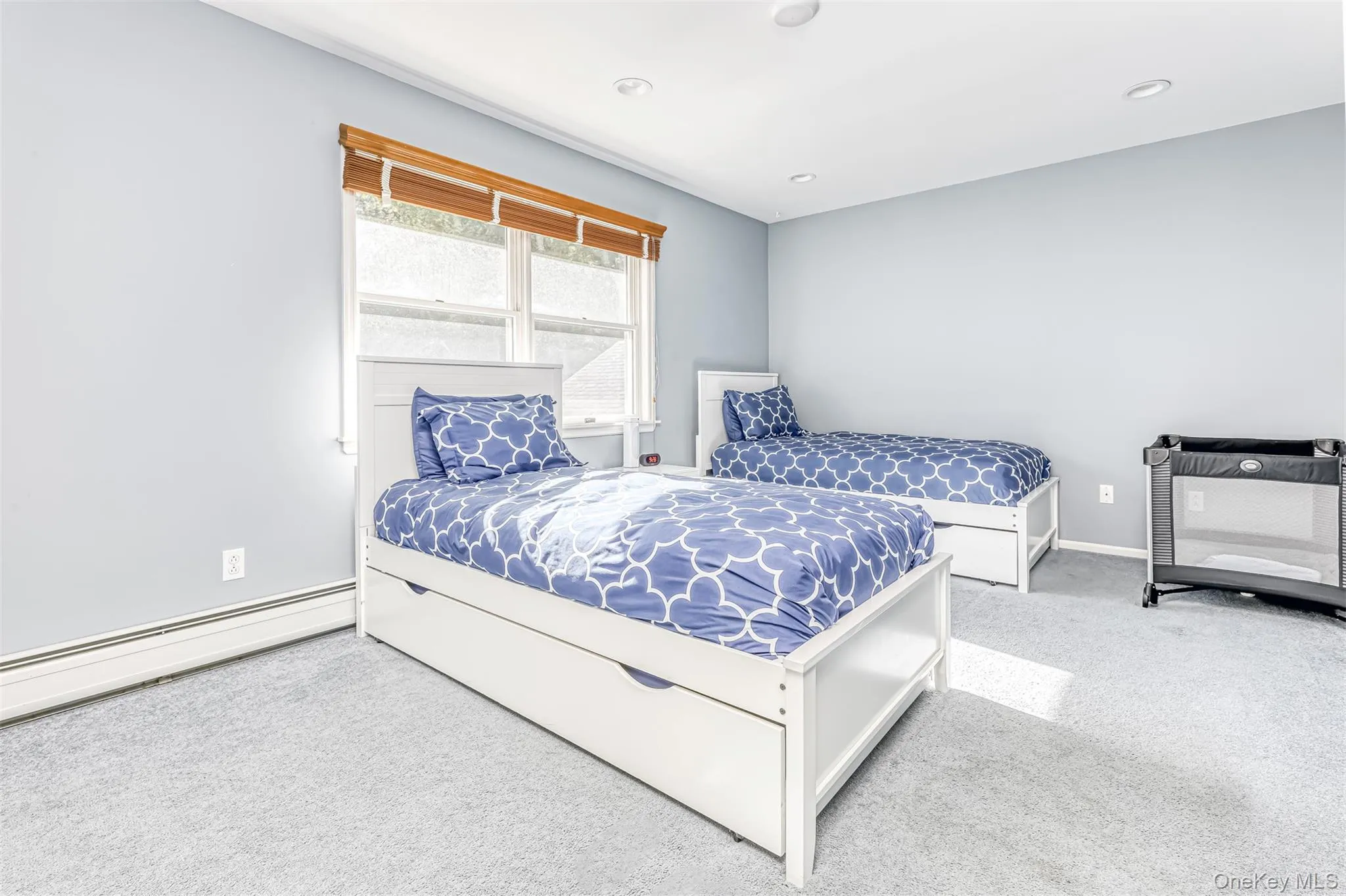 Bright secondary bedroom featuring two twin beds with coordinating blue geometric bedding, white wood-finish bed frames with storage drawers, recessed ceiling lighting, and large windows with natural light Bright secondary bedroom featuring two twin beds with coordinating blue geometric bedding, white wood-finish bed frames with storage drawers, recessed ceiling lighting, and large windows with natural light