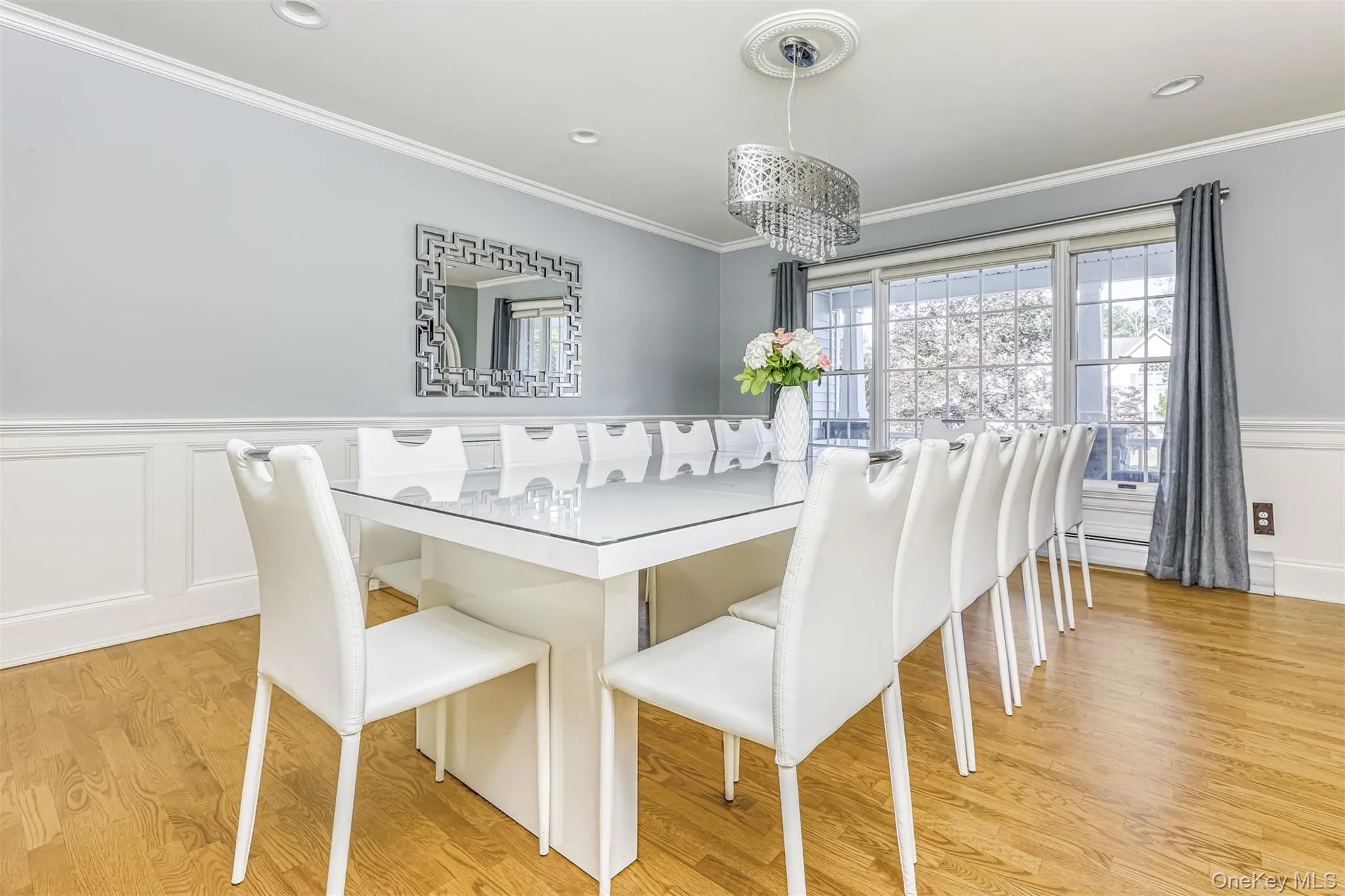 Elegant dining room featuring a white lacquered rectangular table with glass top, eight upholstered dining chairs with white fabric, and a modern crystal pendant light fixture Elegant dining room featuring a white lacquered rectangular table with glass top, eight upholstered dining chairs with white fabric, and a modern crystal pendant light fixture