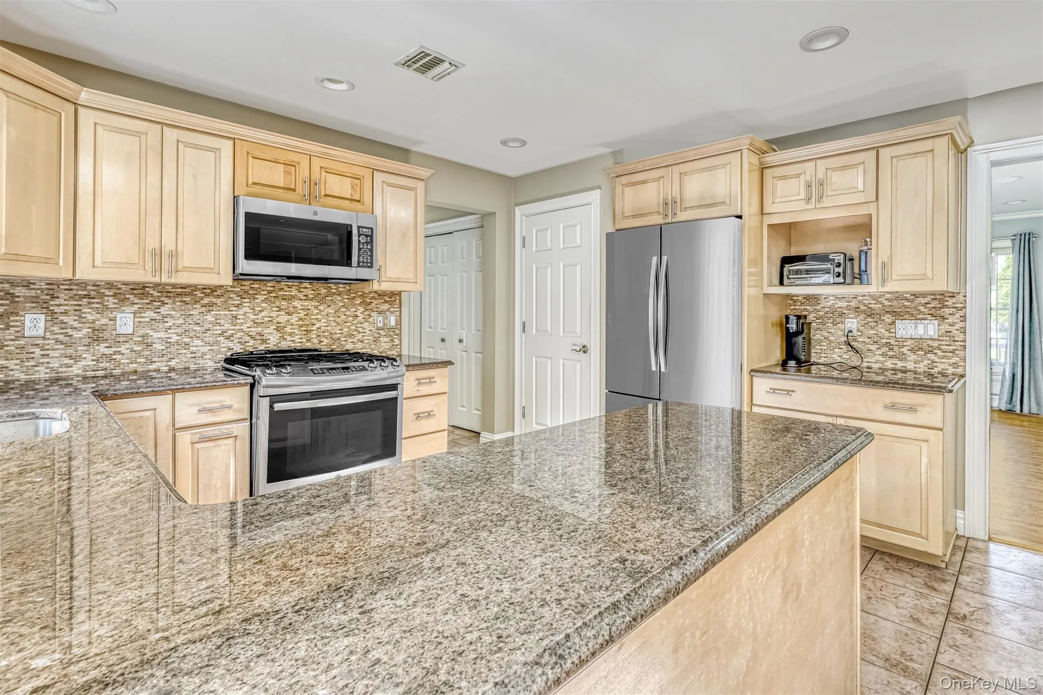 Kitchen featuring light-tone cabinetry, stainless steel appliances, granite countertops, and a full tile backsplash Kitchen featuring light-tone cabinetry, stainless steel appliances, granite countertops, and a full tile backsplash