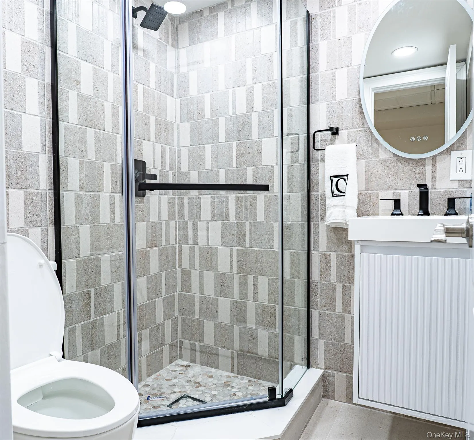 Modern primary bathroom featuring a frameless glass walk-in shower enclosure with matte black hardware and a linear showerhead, subway tile walls in neutral tones arranged in a stacked pattern, and a terrazzo tile shower floor Modern primary bathroom featuring a frameless glass walk-in shower enclosure with matte black hardware and a linear showerhead, subway tile walls in neutral tones arranged in a stacked pattern, and a terrazzo tile shower floor