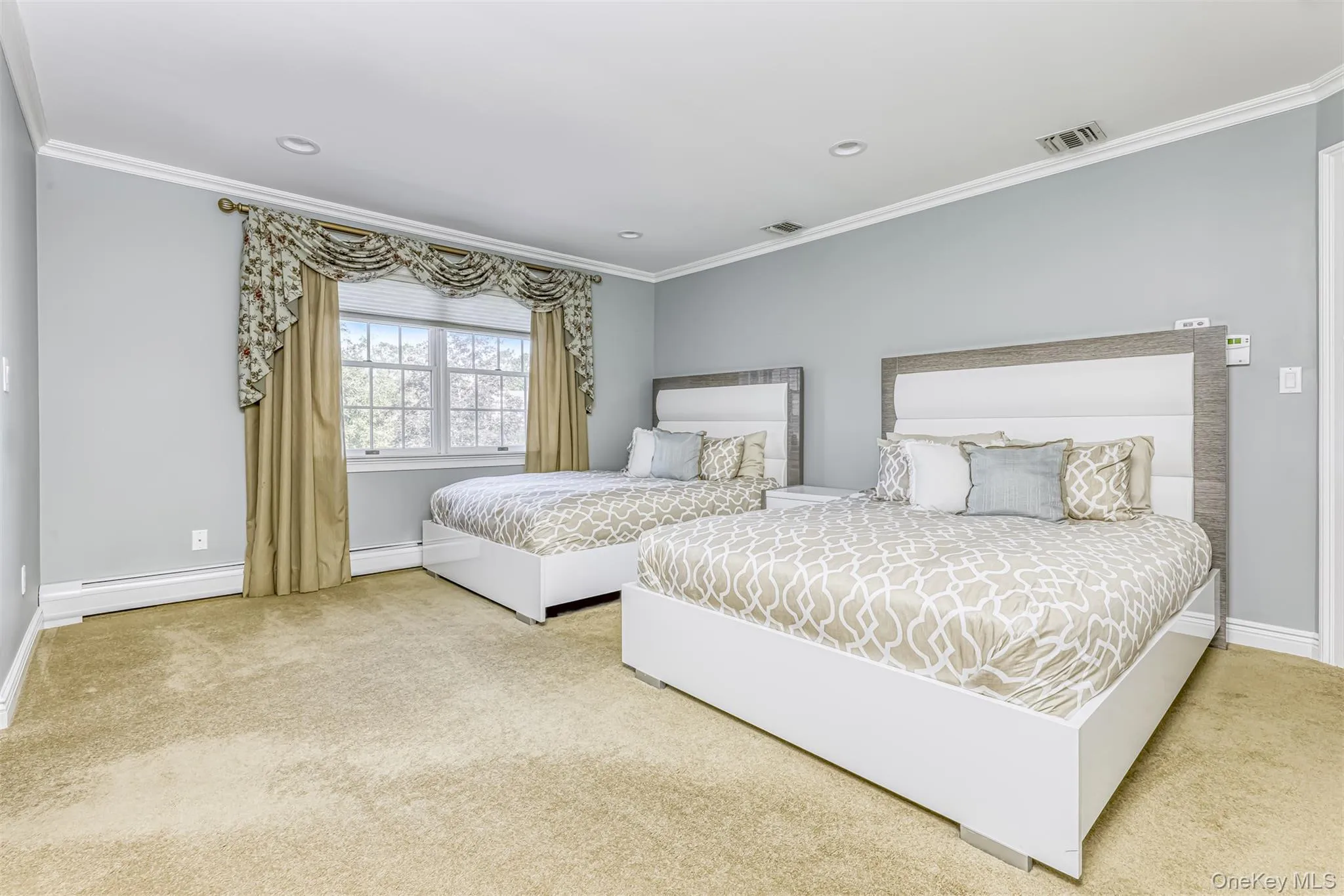Spacious guest bedroom featuring two full beds with upholstered headboards, neutral wall finishes, recessed ceiling lighting, carpeted flooring, and large multi-pane windows with coordinating drapery and natural light access Spacious guest bedroom featuring two full beds with upholstered headboards, neutral wall finishes, recessed ceiling lighting, carpeted flooring, and large multi-pane windows with coordinating drapery and natural light access